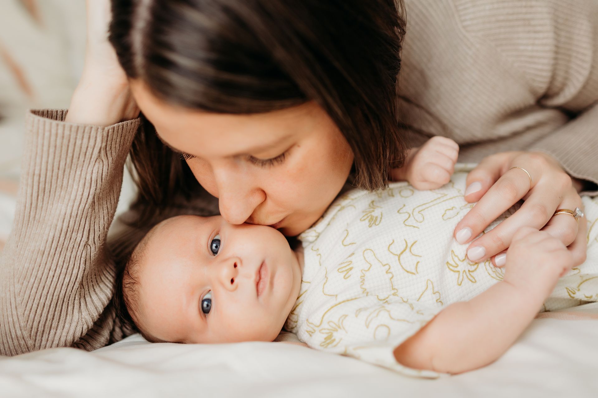A woman is kissing her newborn baby on the cheek.
