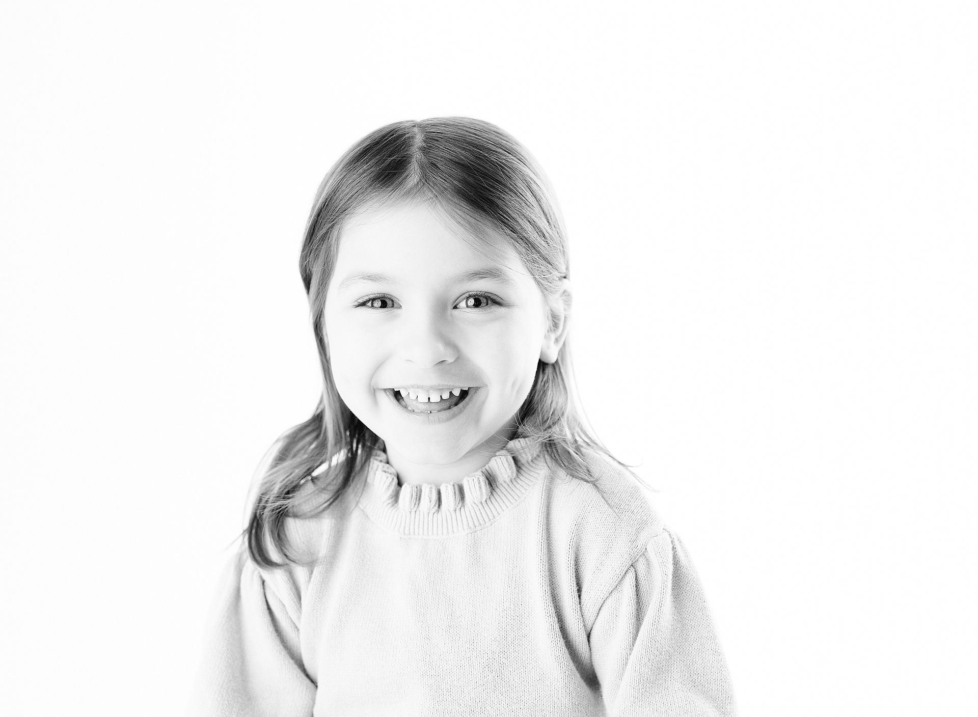 Smiling child wearing a light-colored sweater, with long hair, against a white background.