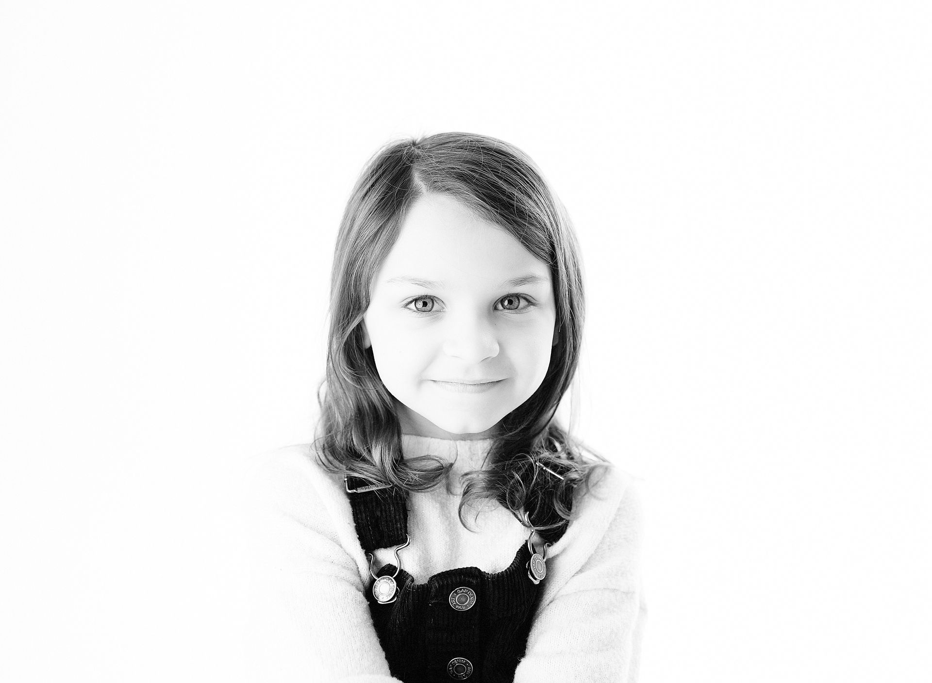 Girl smiling, wearing overalls, against a white background.