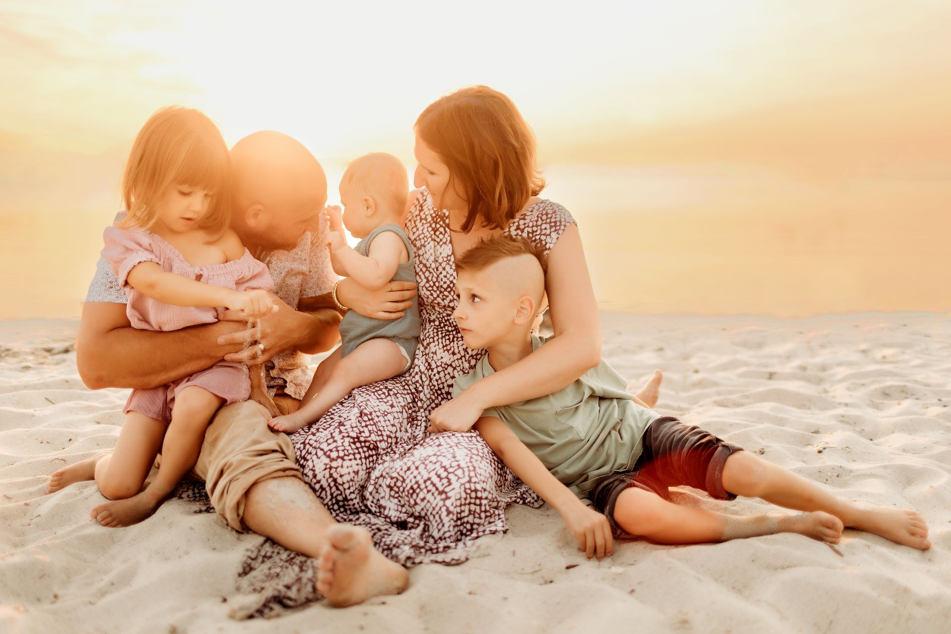 Family sitting on a sandy beach at sunset, interacting playfully.
