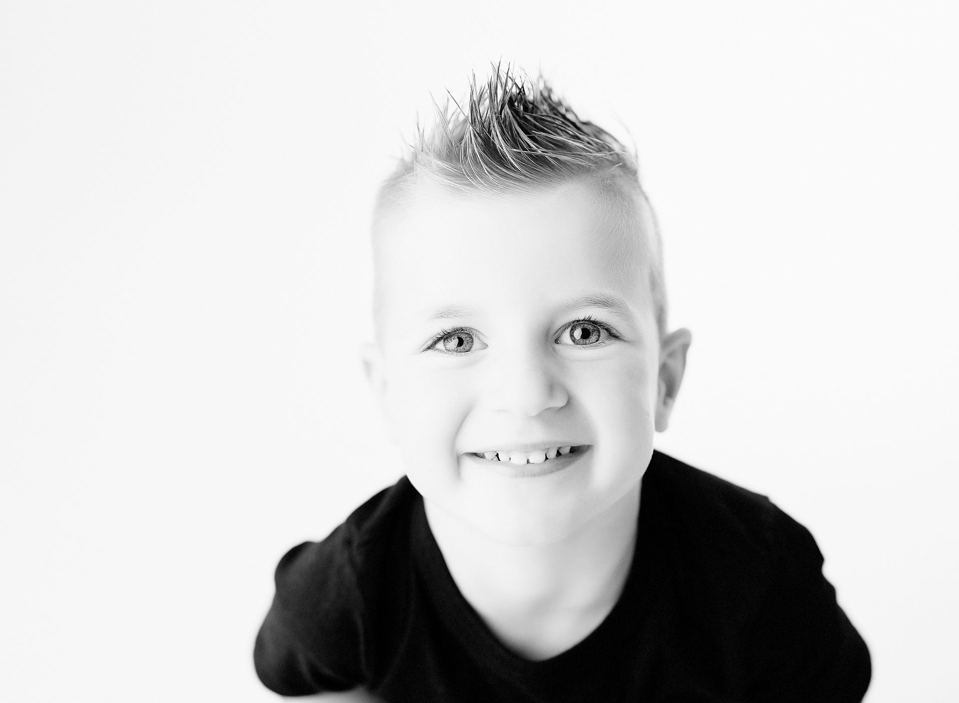 Boy with a spiky haircut, smiling, wearing a black shirt, against a white background.