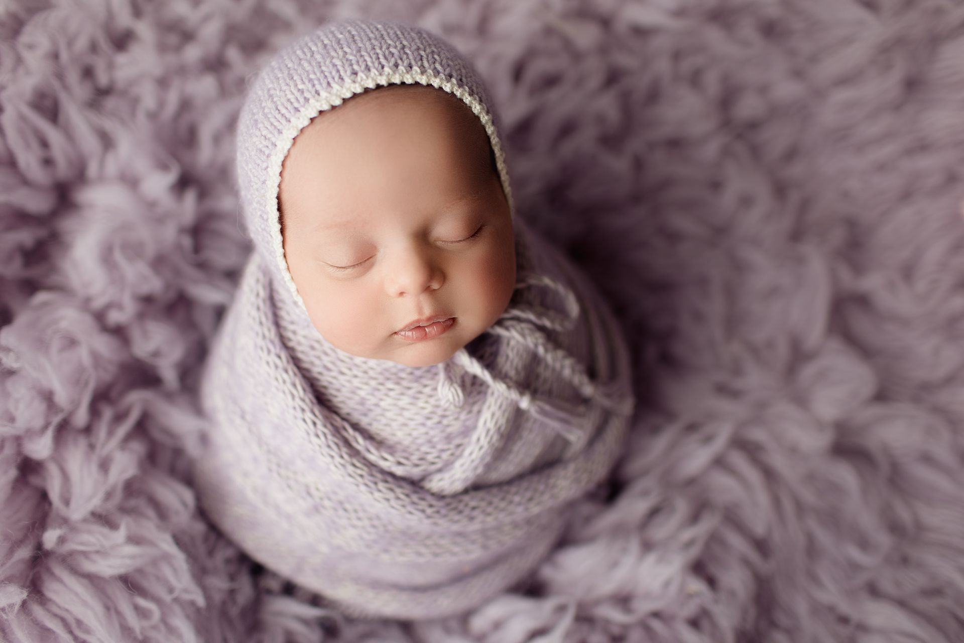 A newborn baby is wrapped in a purple blanket and wearing a hat.