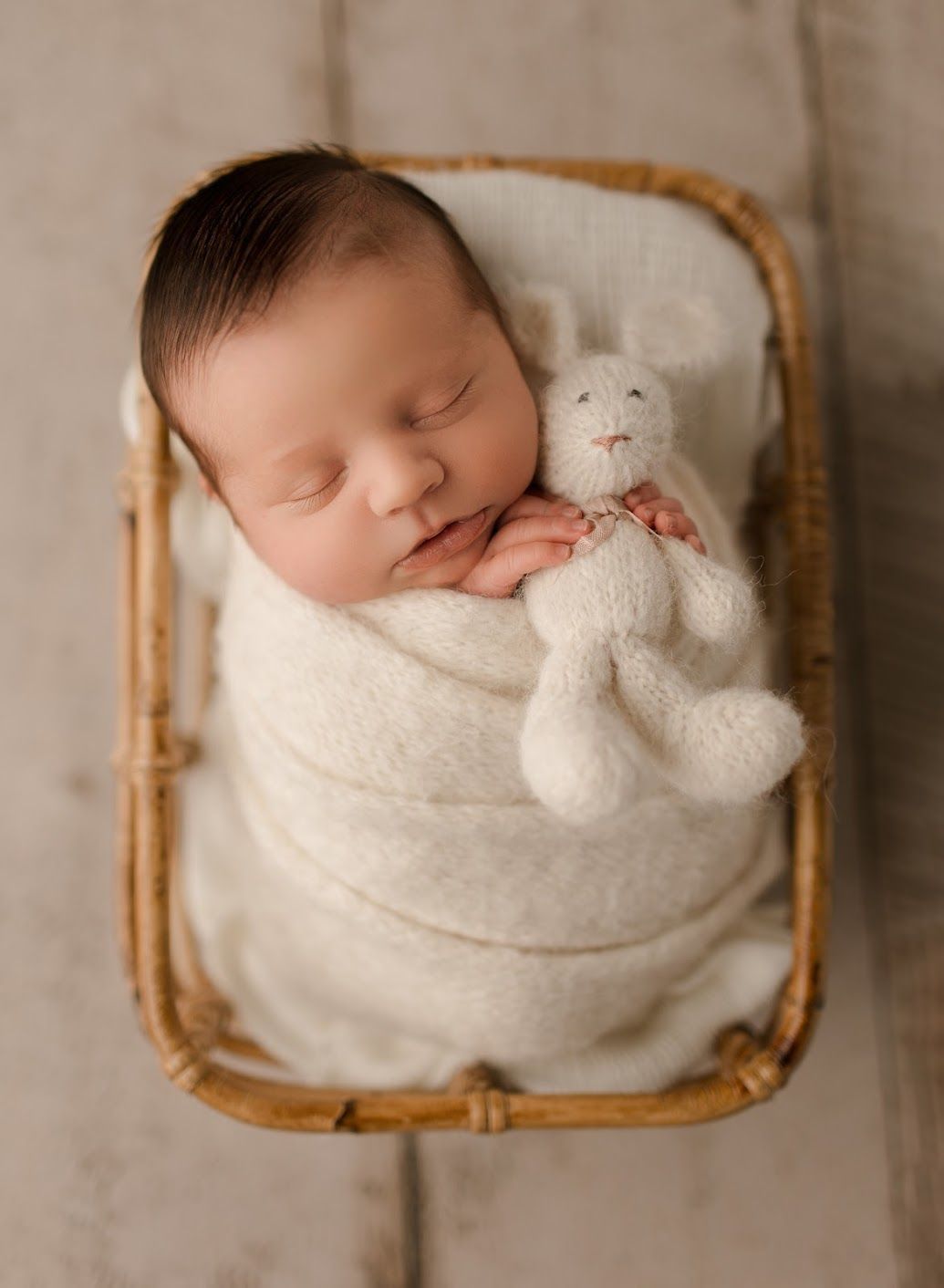 A newborn baby is sleeping in a wicker basket holding a stuffed bunny.