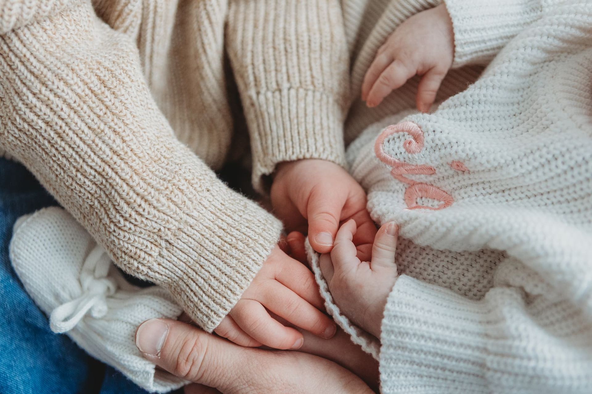 A close-up view of hands holding together, featuring knitted sweaters and a baby’s embroidered garment.