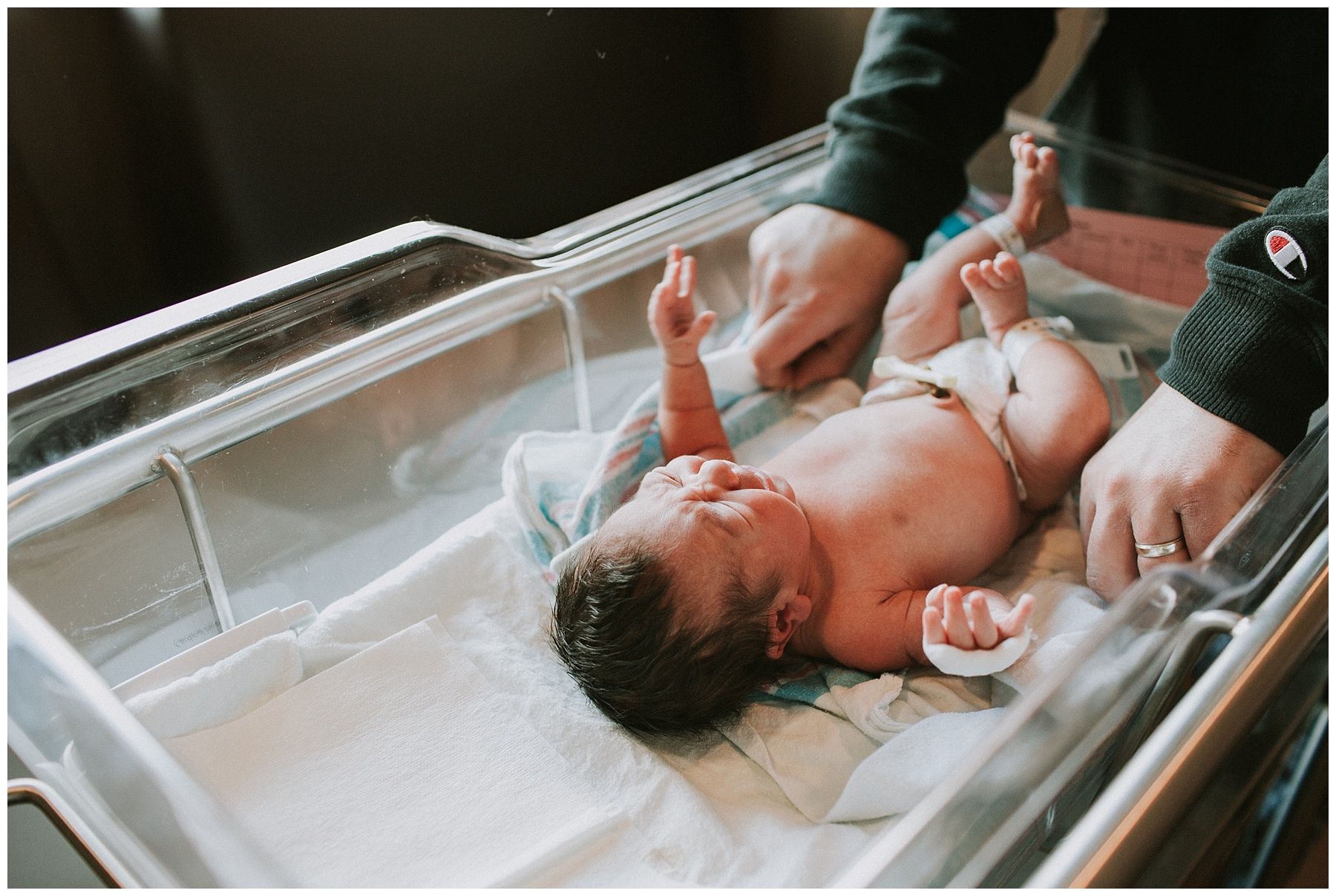 A man is changing a newborn baby 's diaper in a hospital crib.