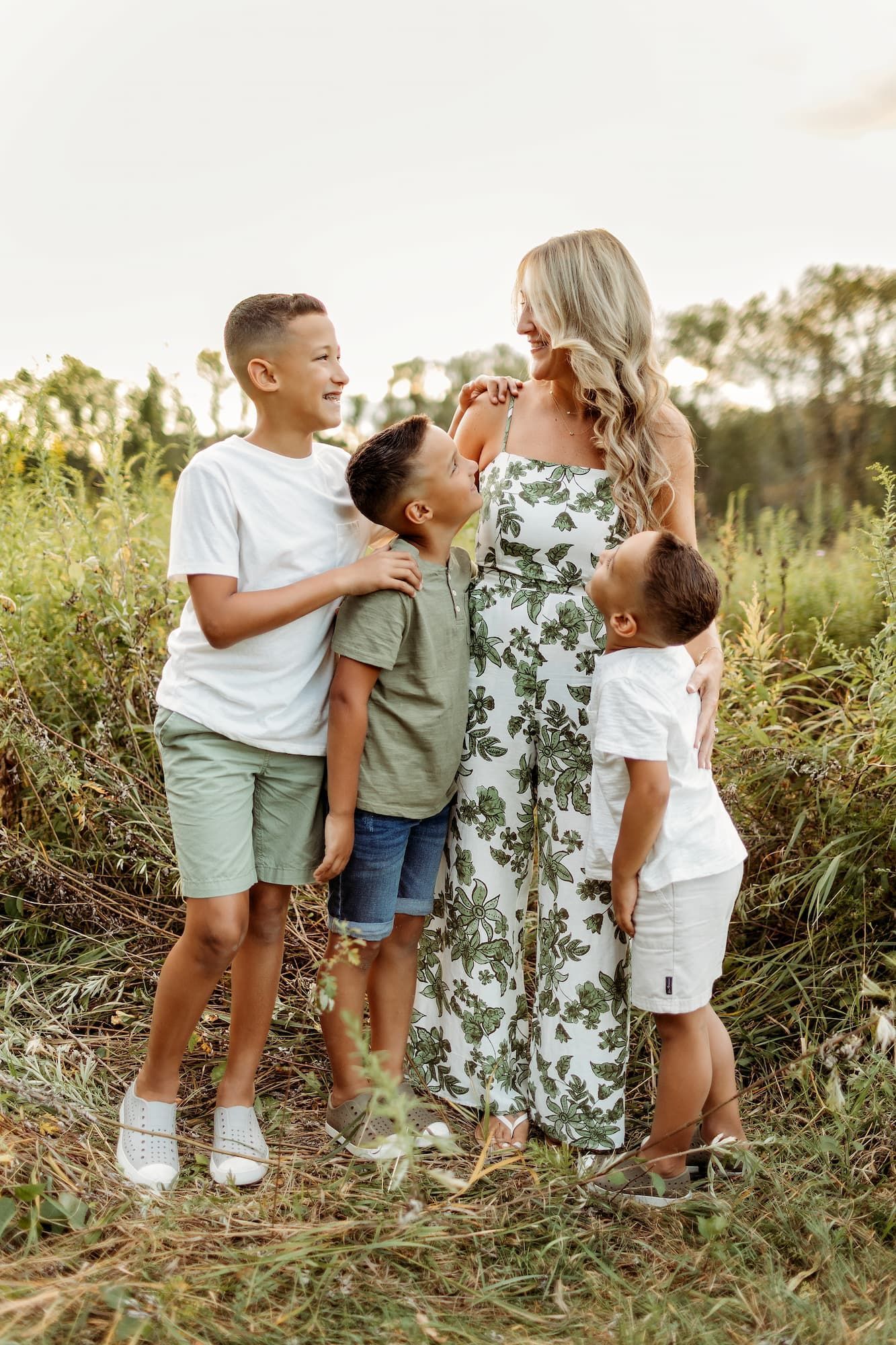 Woman in floral jumpsuit with three children in an outdoor setting. They are looking at each other and smiling.