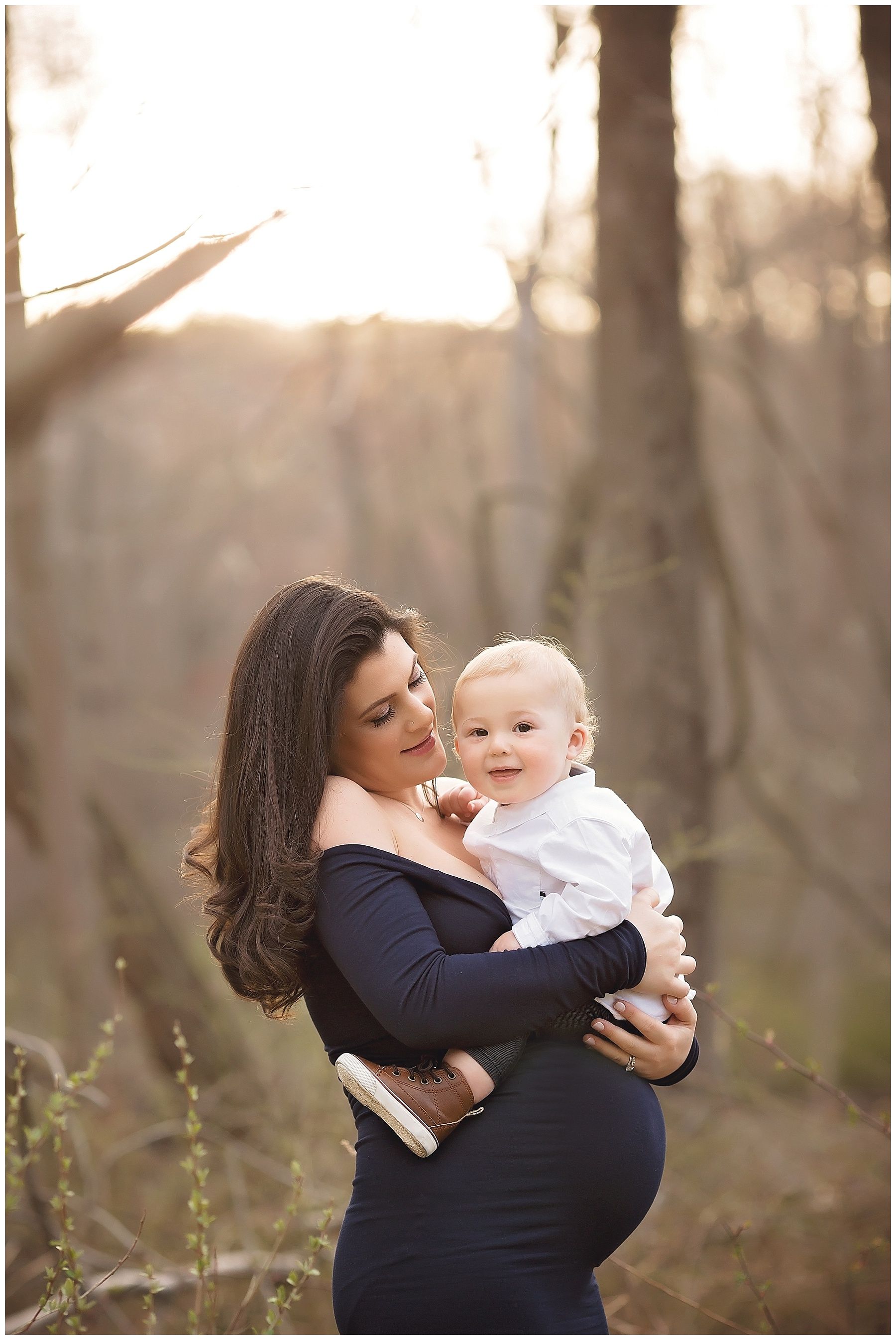 A pregnant woman is holding a baby in her arms in the woods.