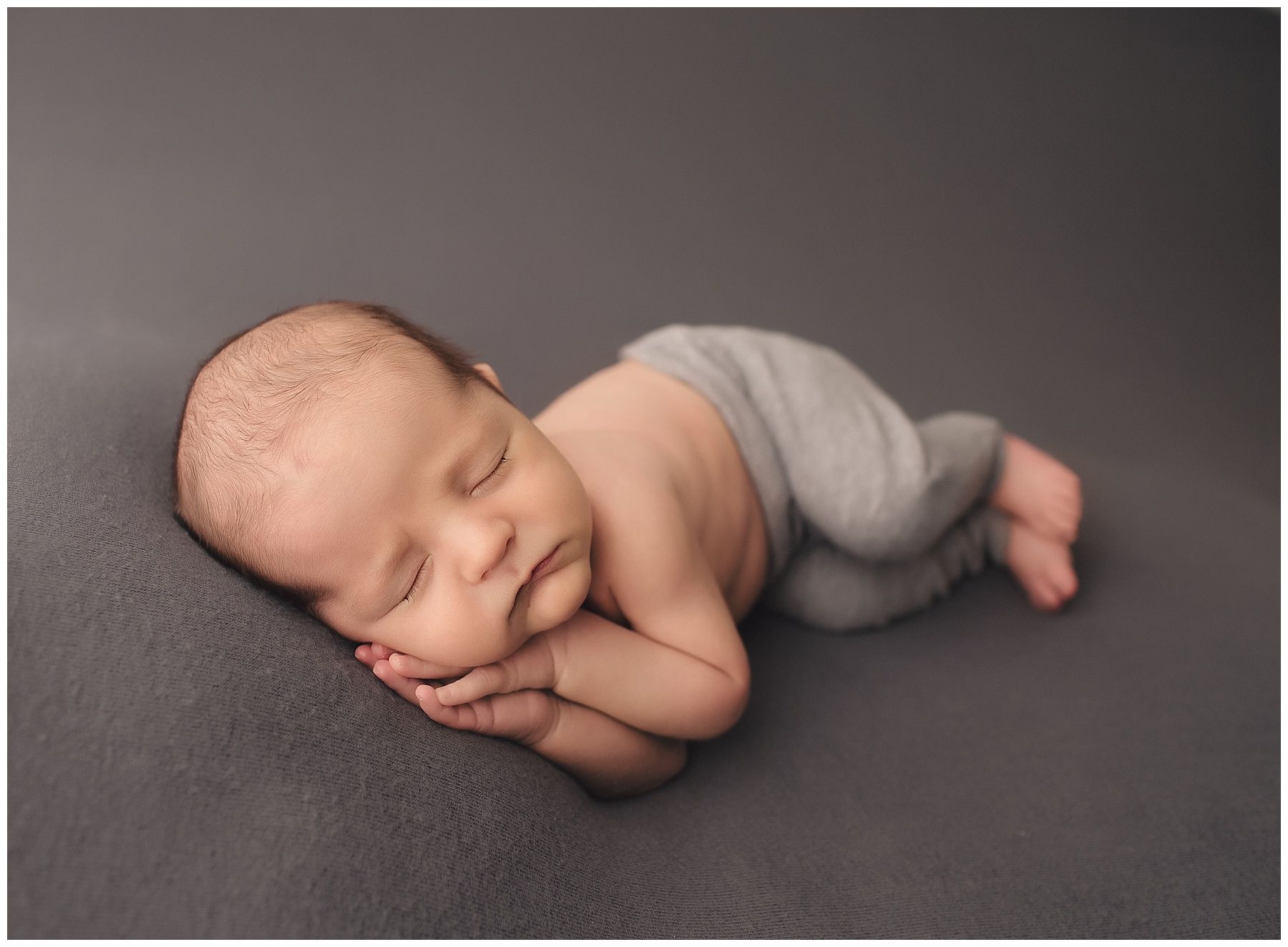 A newborn baby is sleeping on a gray blanket.