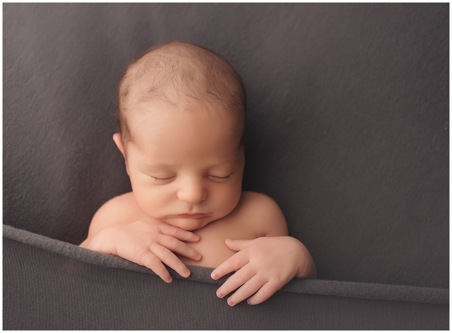 A newborn baby is sleeping on a gray blanket.