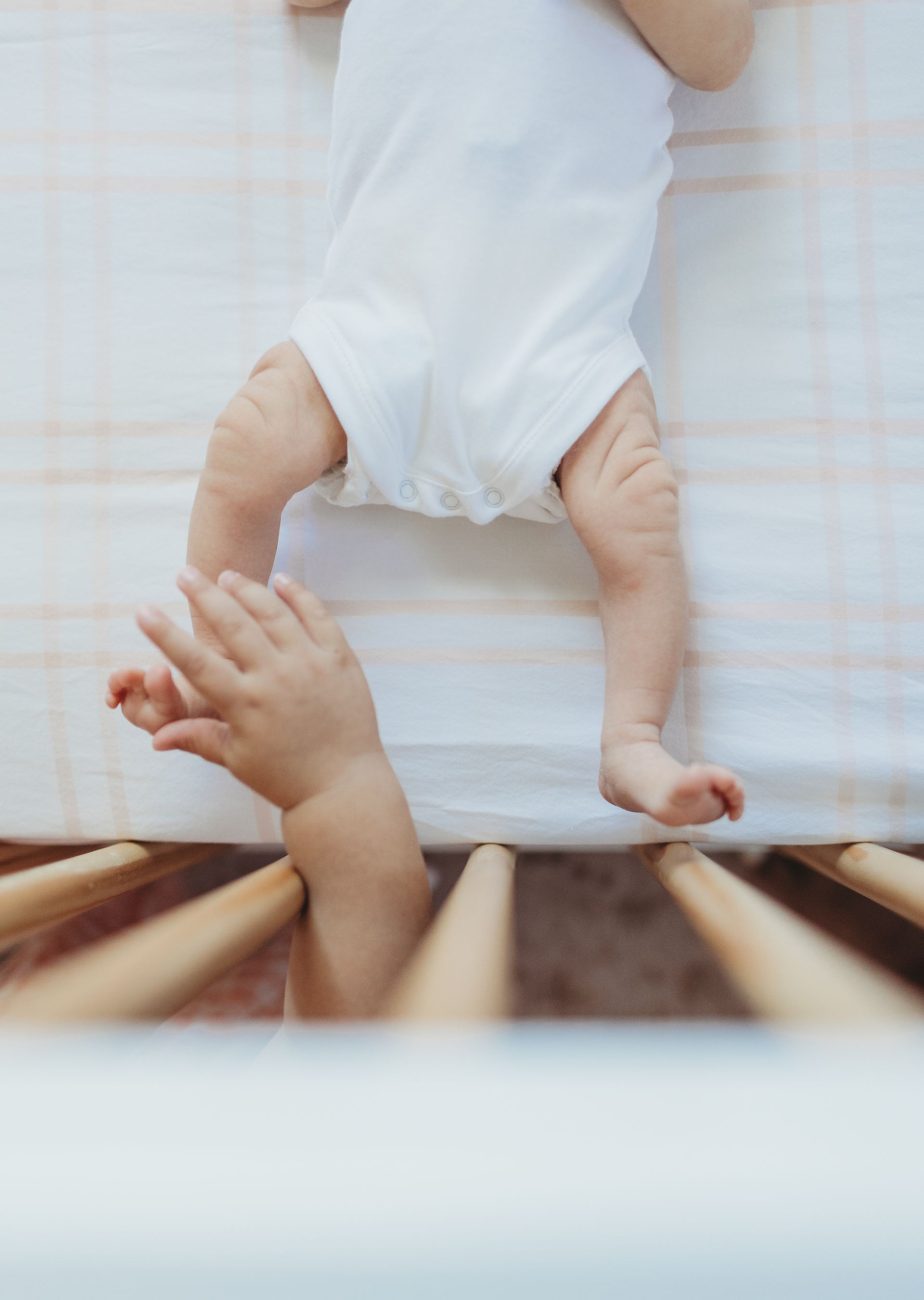 A baby is laying in a crib and a baby is reaching for it.