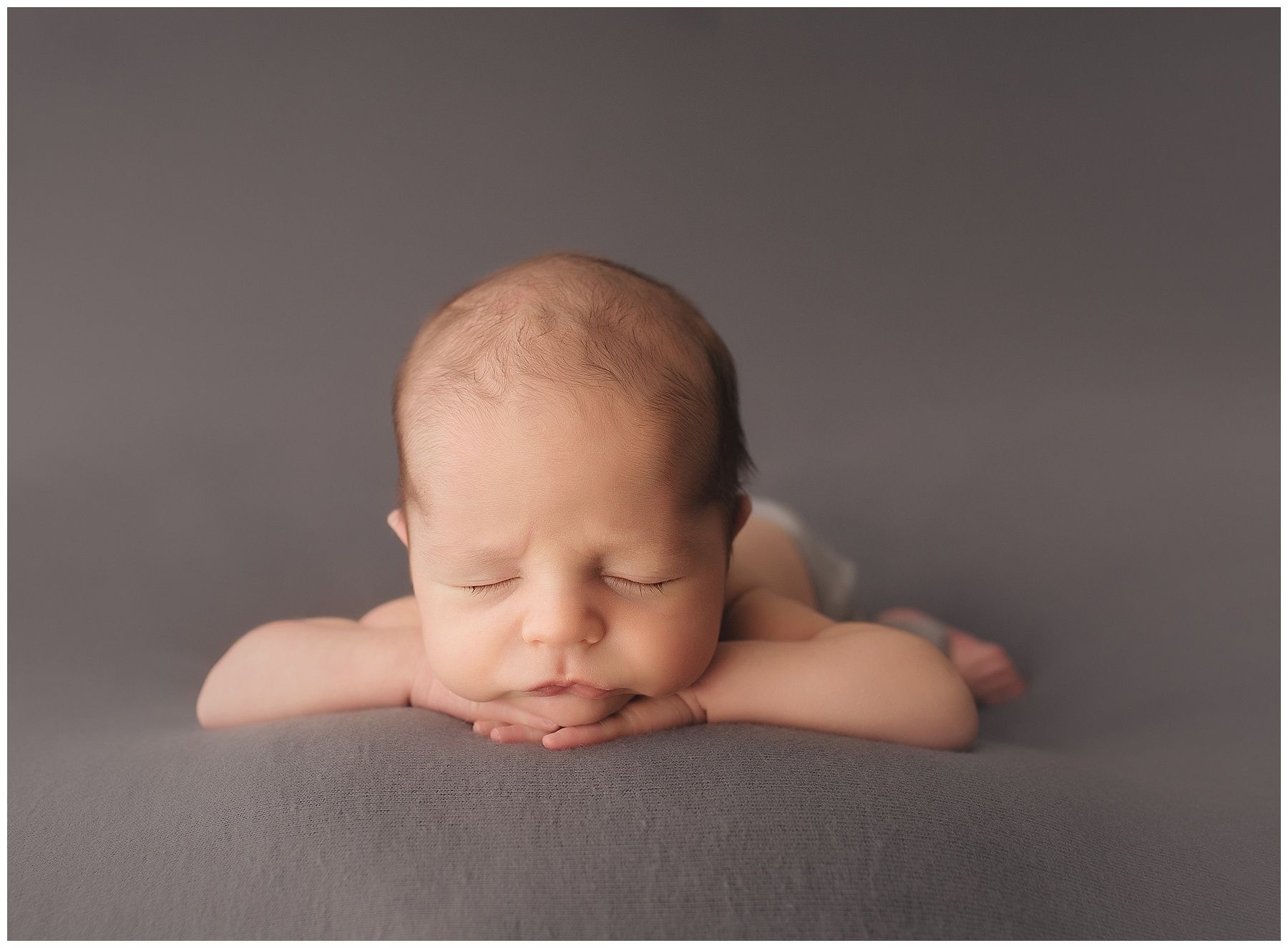 A newborn baby is laying on his stomach with his head resting on his hands.