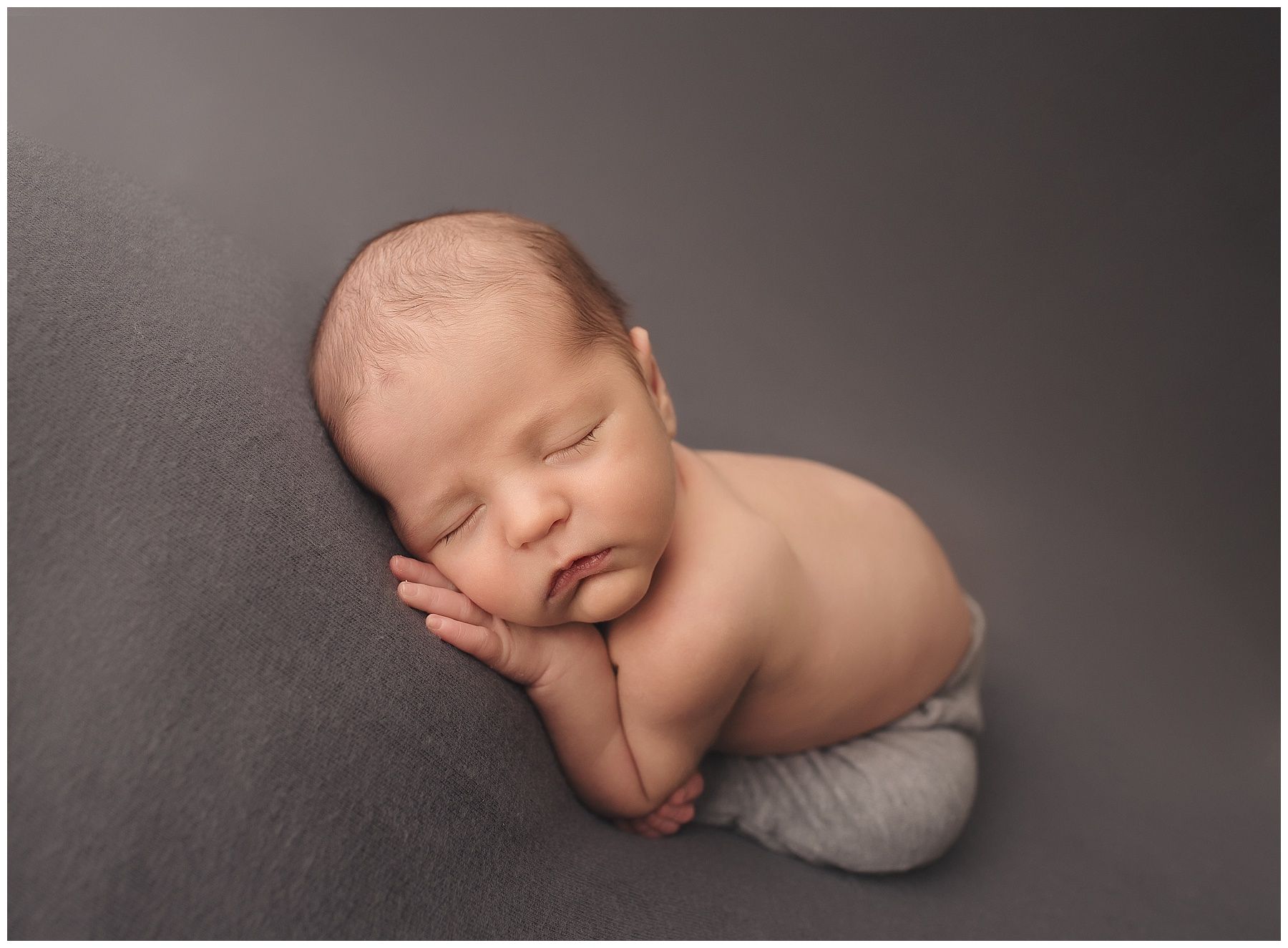 A newborn baby is sleeping on a gray blanket.