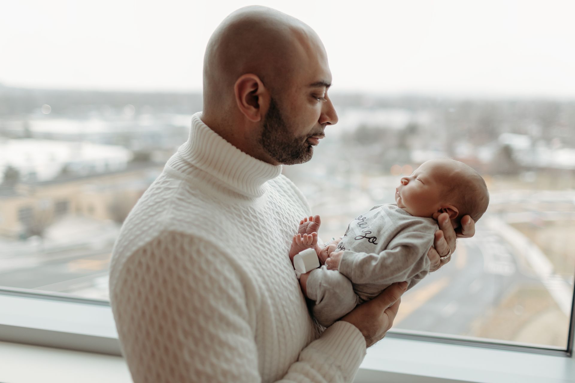 A man is holding a baby in his arms in front of a window.