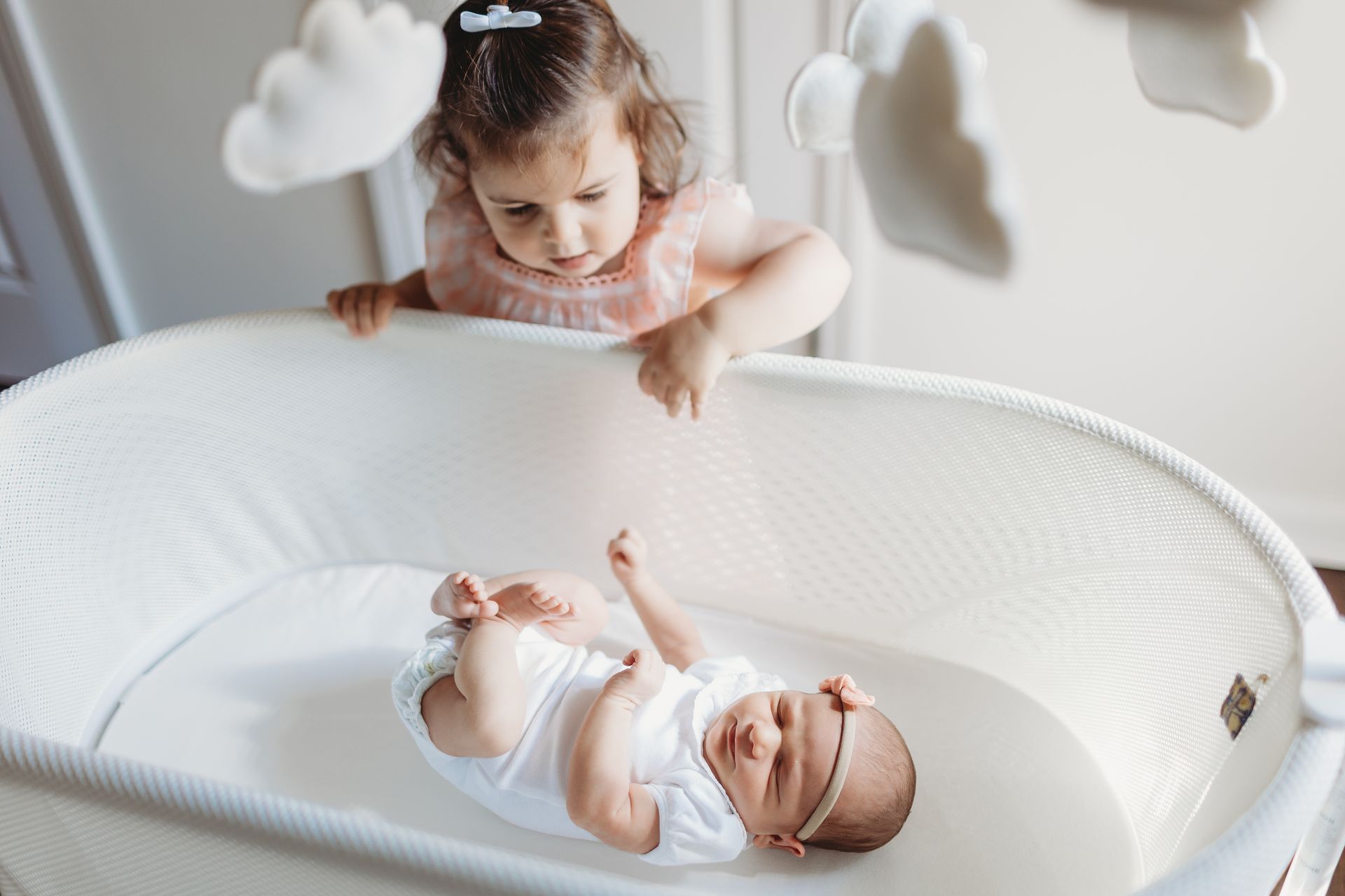 A little girl is standing next to a baby in a crib.