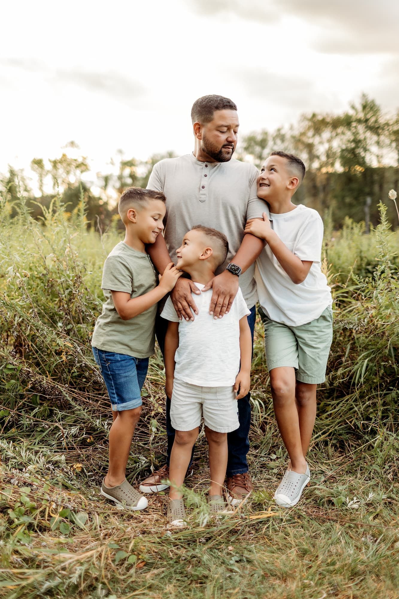 A man stands with three boys in a field, smiling, embracing.