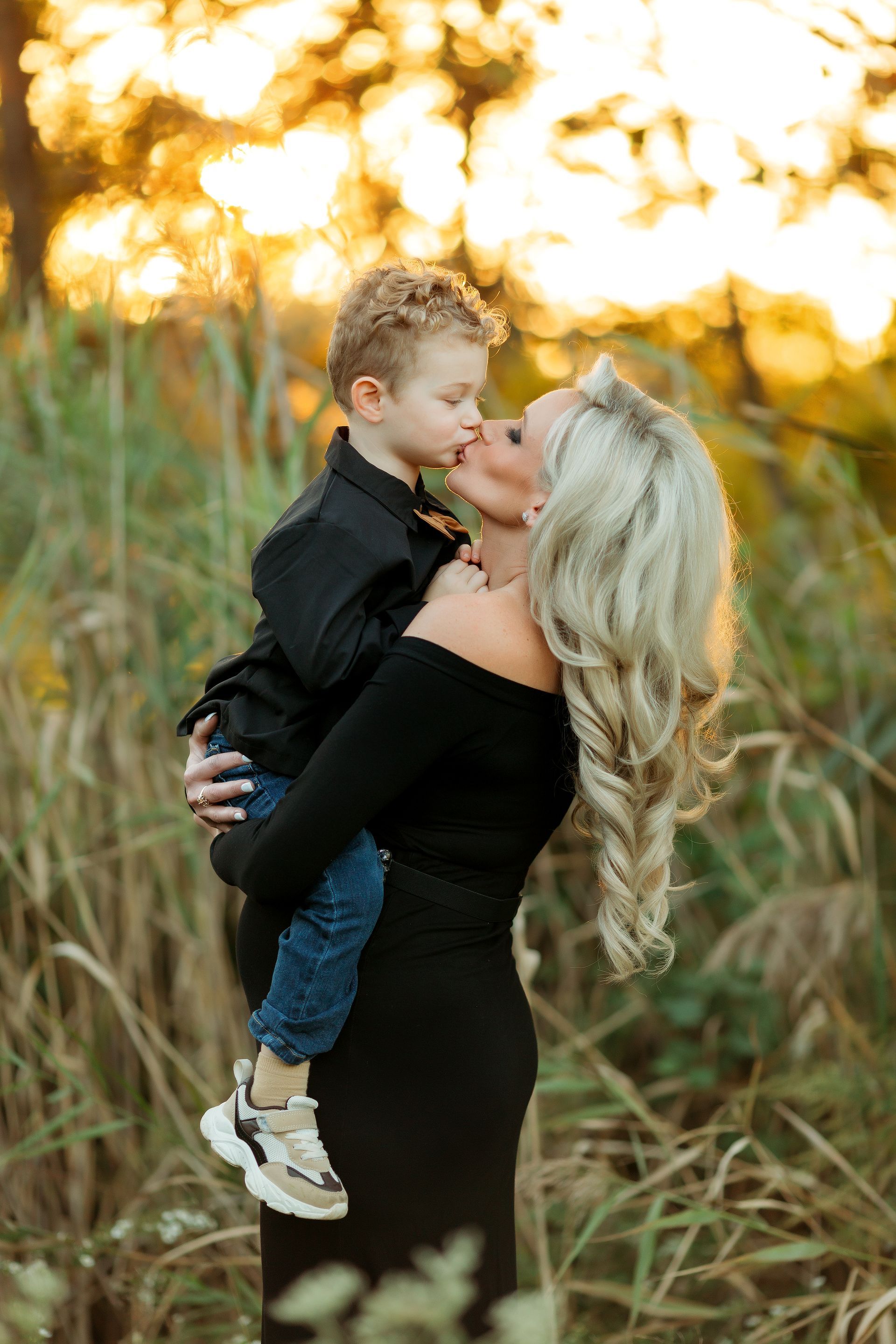 A woman is holding a child in her arms and kissing him on the cheek.