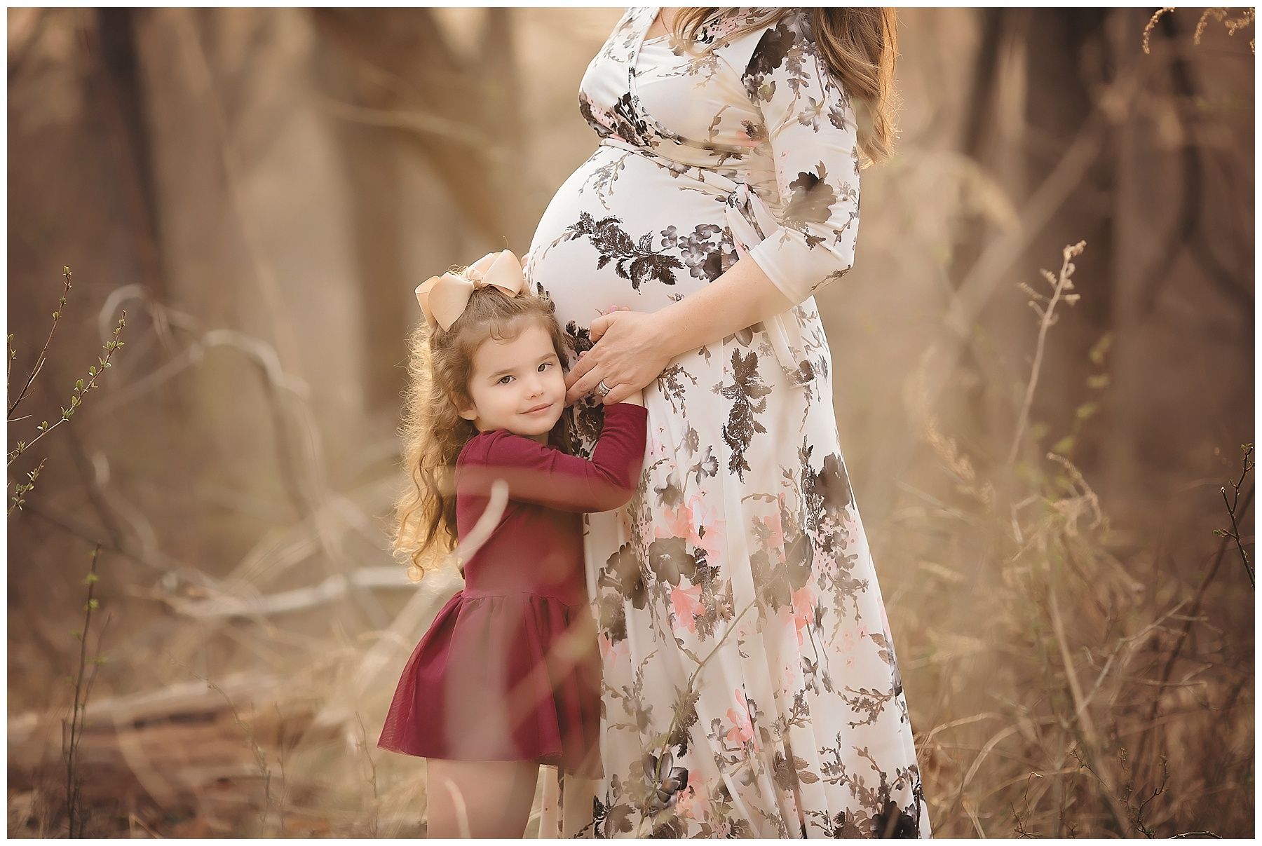 A little girl is hugging a pregnant woman in a field.