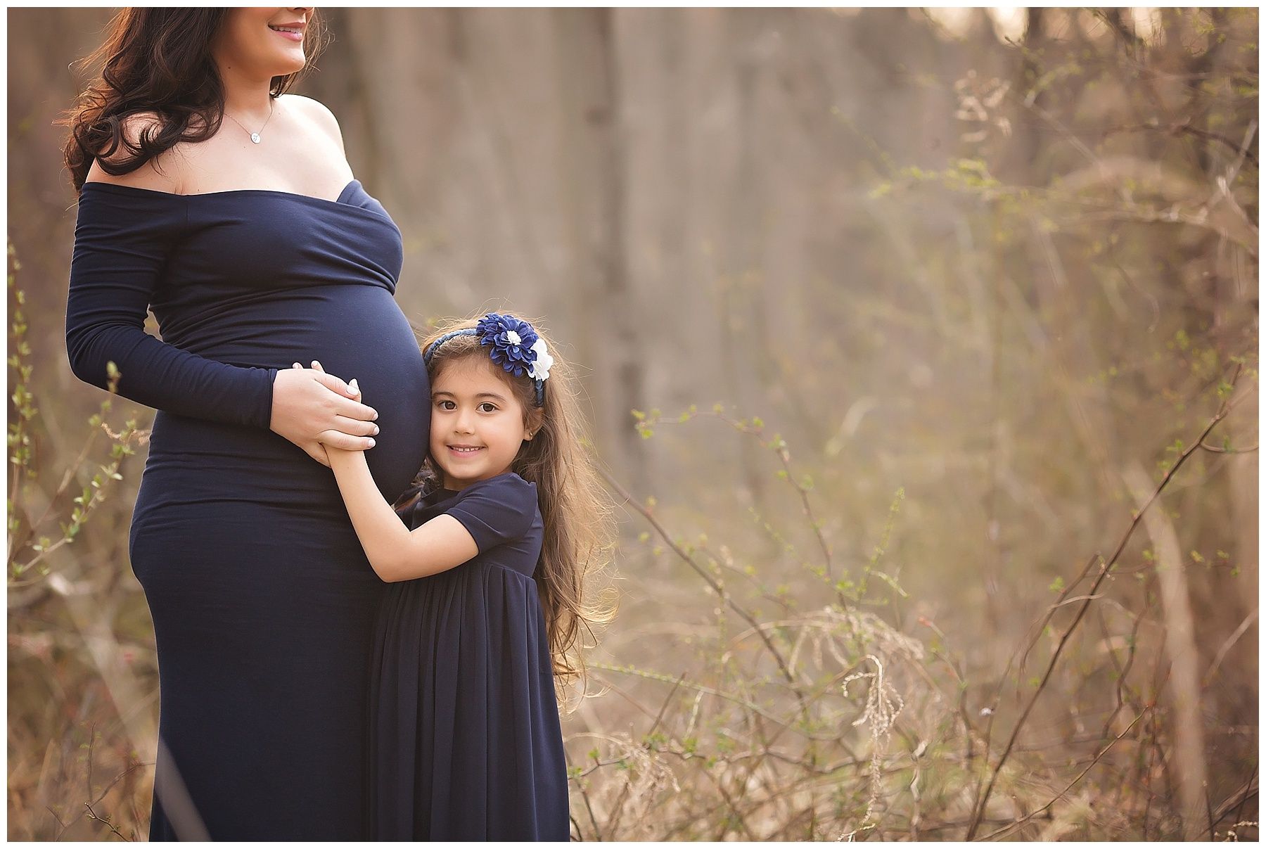 A pregnant woman in a blue dress is standing next to a little girl in a blue dress.