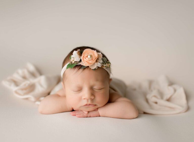 A newborn baby girl wearing a flower headband is sleeping on a bed.