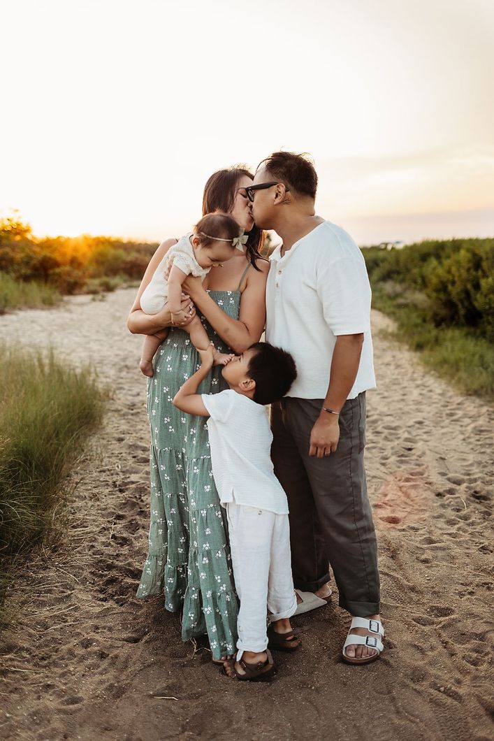 Family smiling at amusement park, father holding child, mother embracing two children.