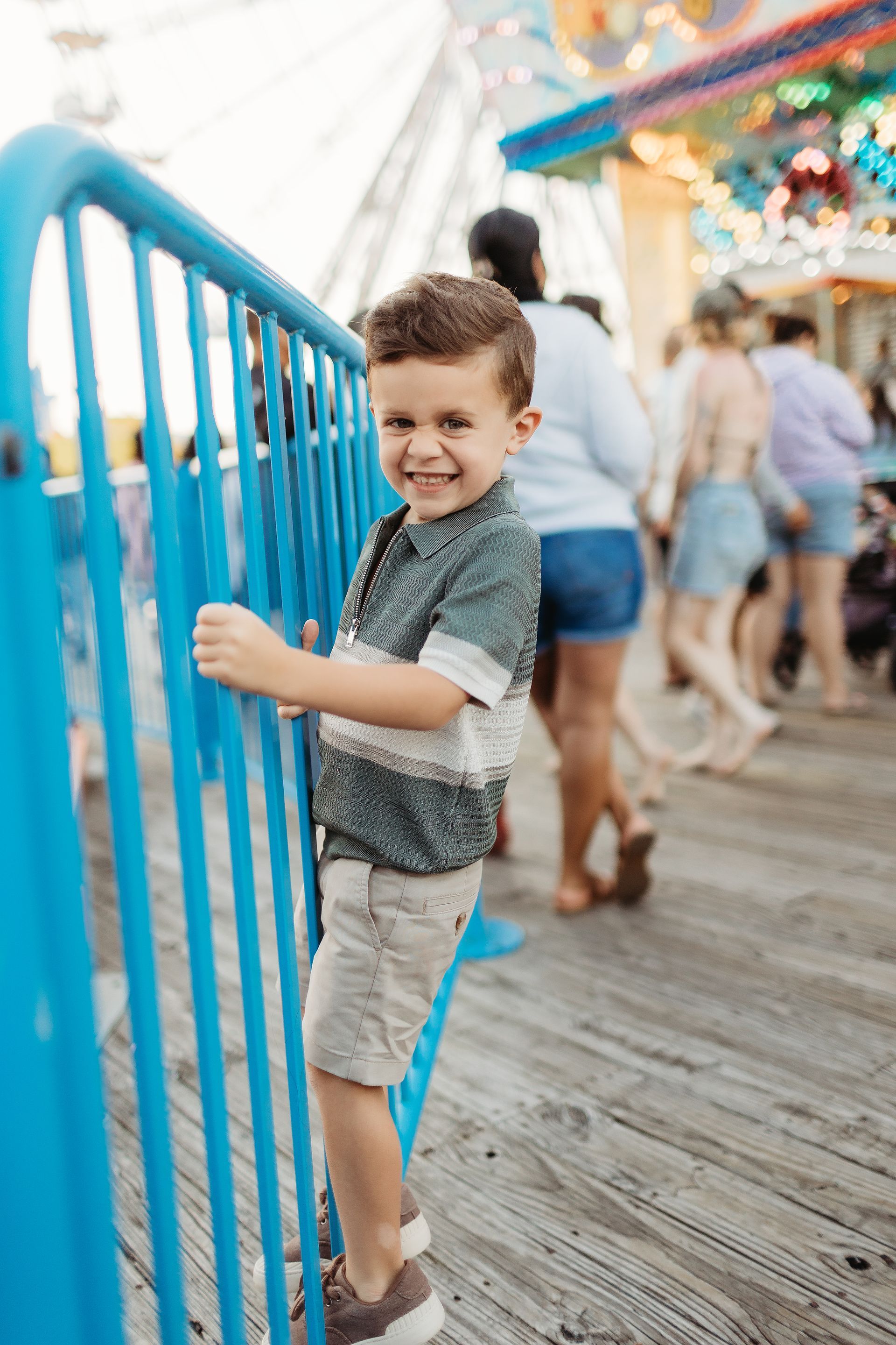 Smiling young boy leans on blue barrier at amusement park.
