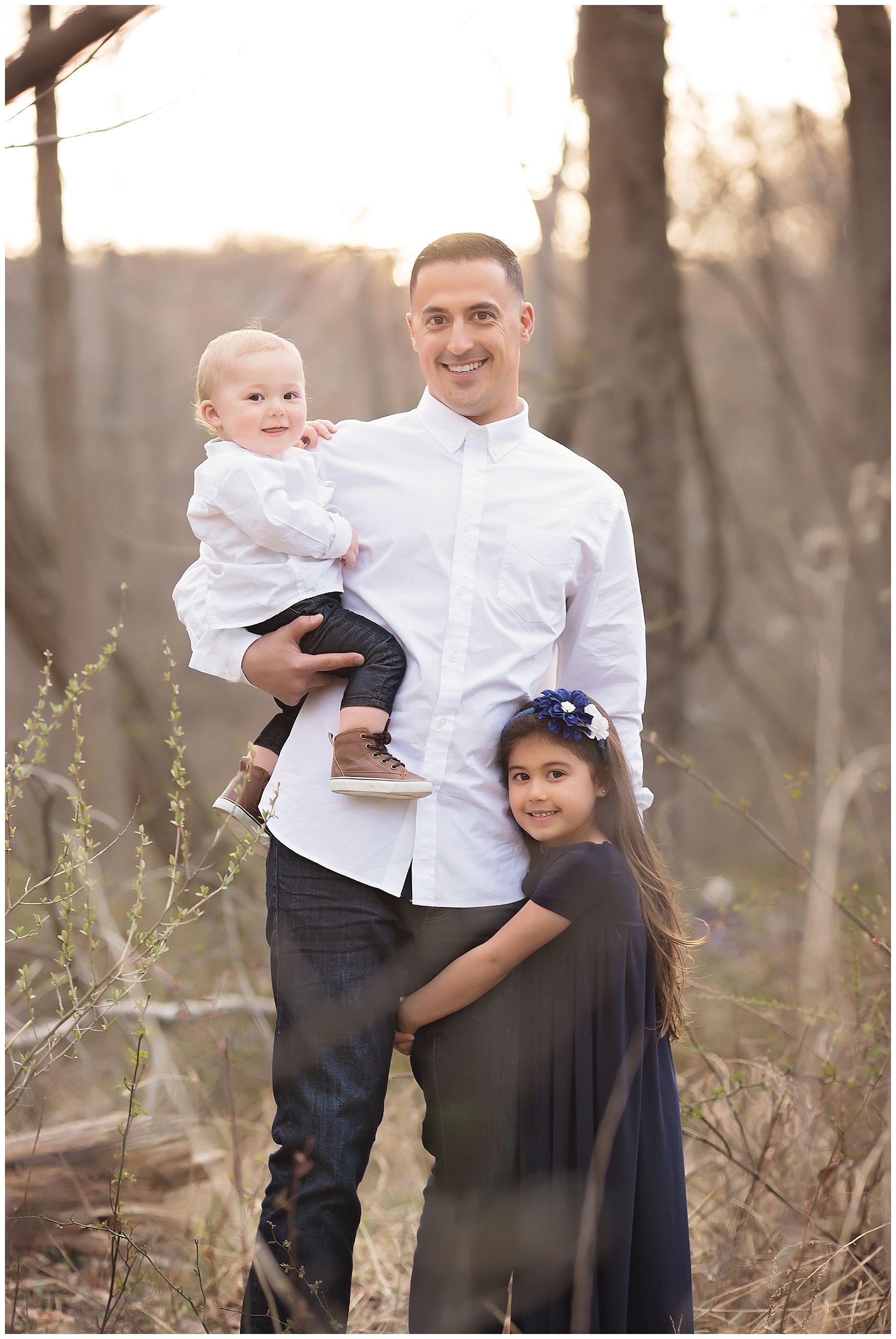 A man is holding a baby and a girl in a field.