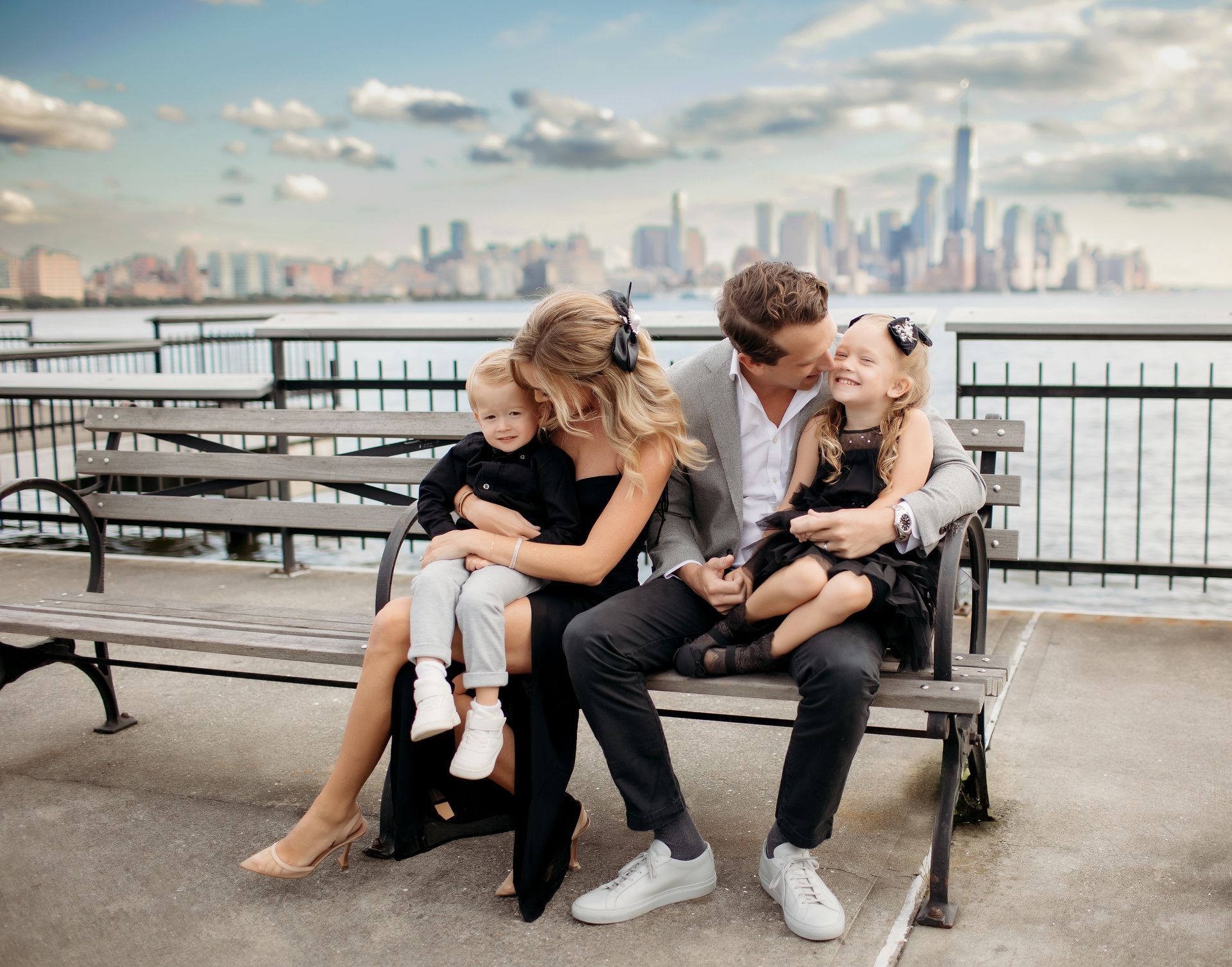 A family is sitting on a bench in front of New York City Skyline.