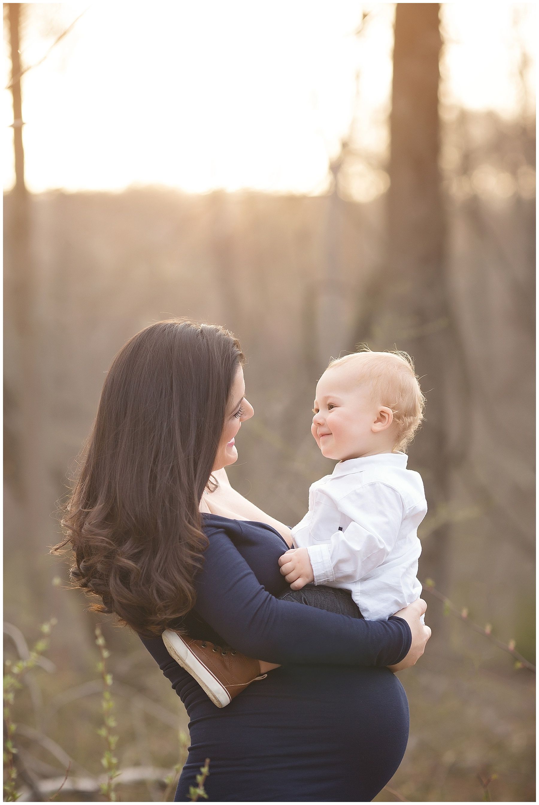 A pregnant woman is holding a baby in her arms in the woods.