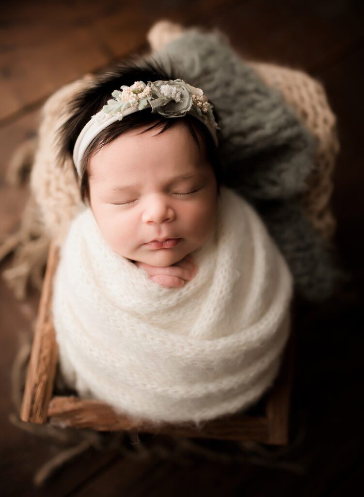 A newborn baby wrapped in a white blanket is sleeping in a wooden crate.