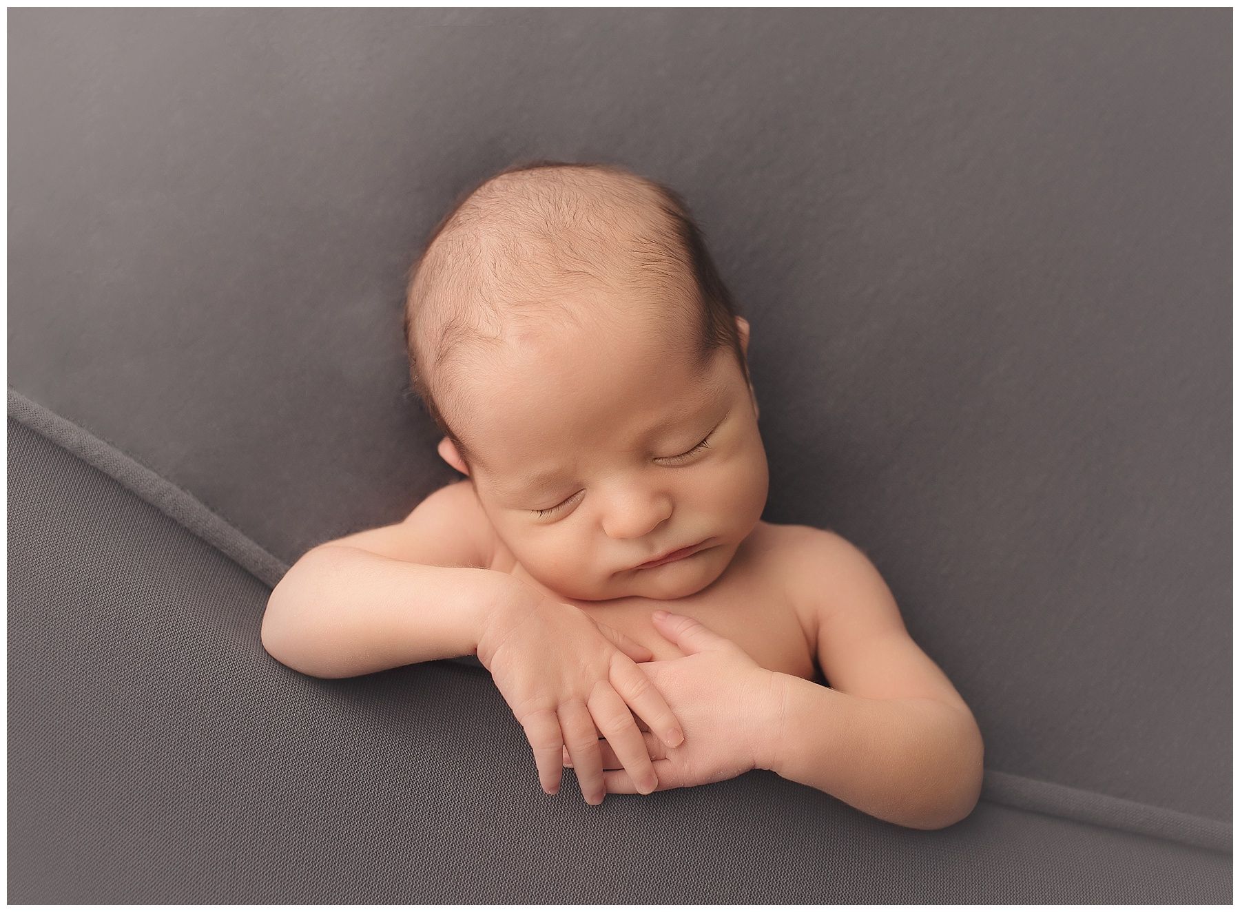 A newborn baby is sleeping on a gray blanket.