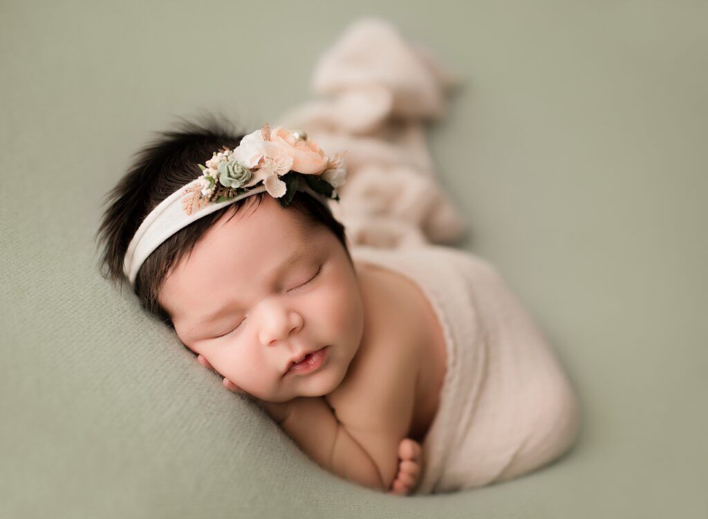 A newborn baby is wrapped in a blanket and wearing a headband.