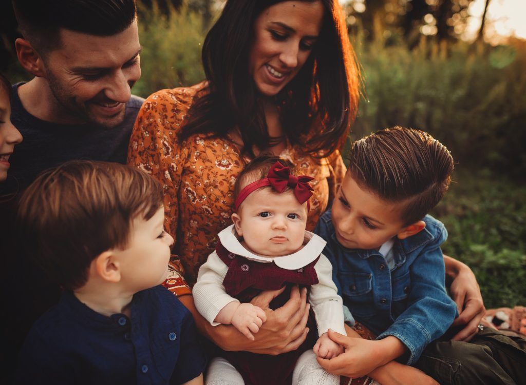 A family is sitting in the grass with a baby in their arms.