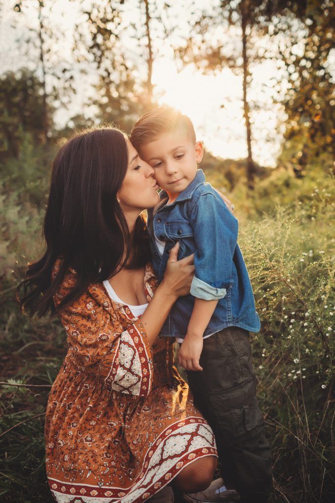 A woman is kissing her son on the cheek in a field.