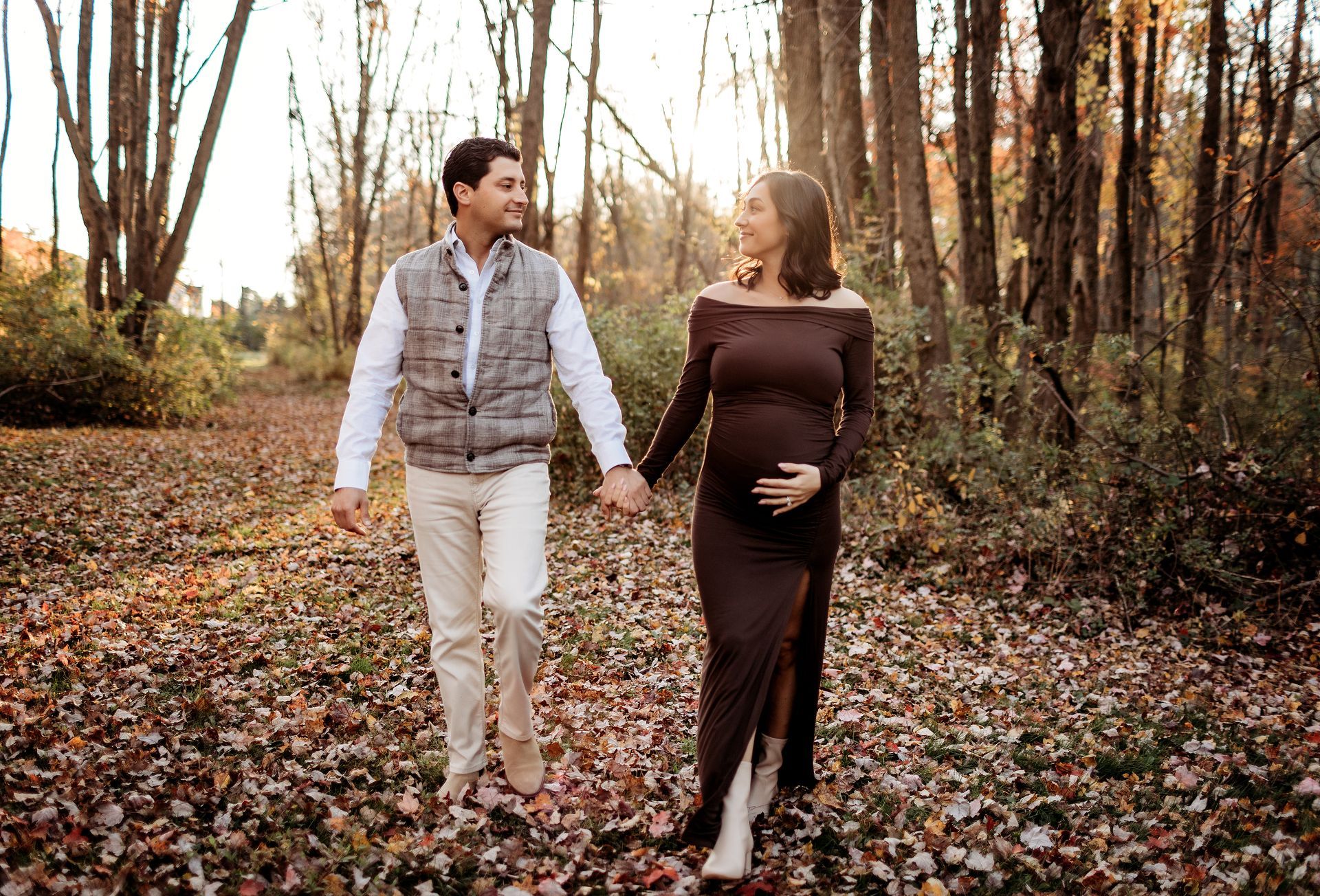 Couple walking hand-in-hand in a forest, smiling. The woman is pregnant. Autumn leaves.