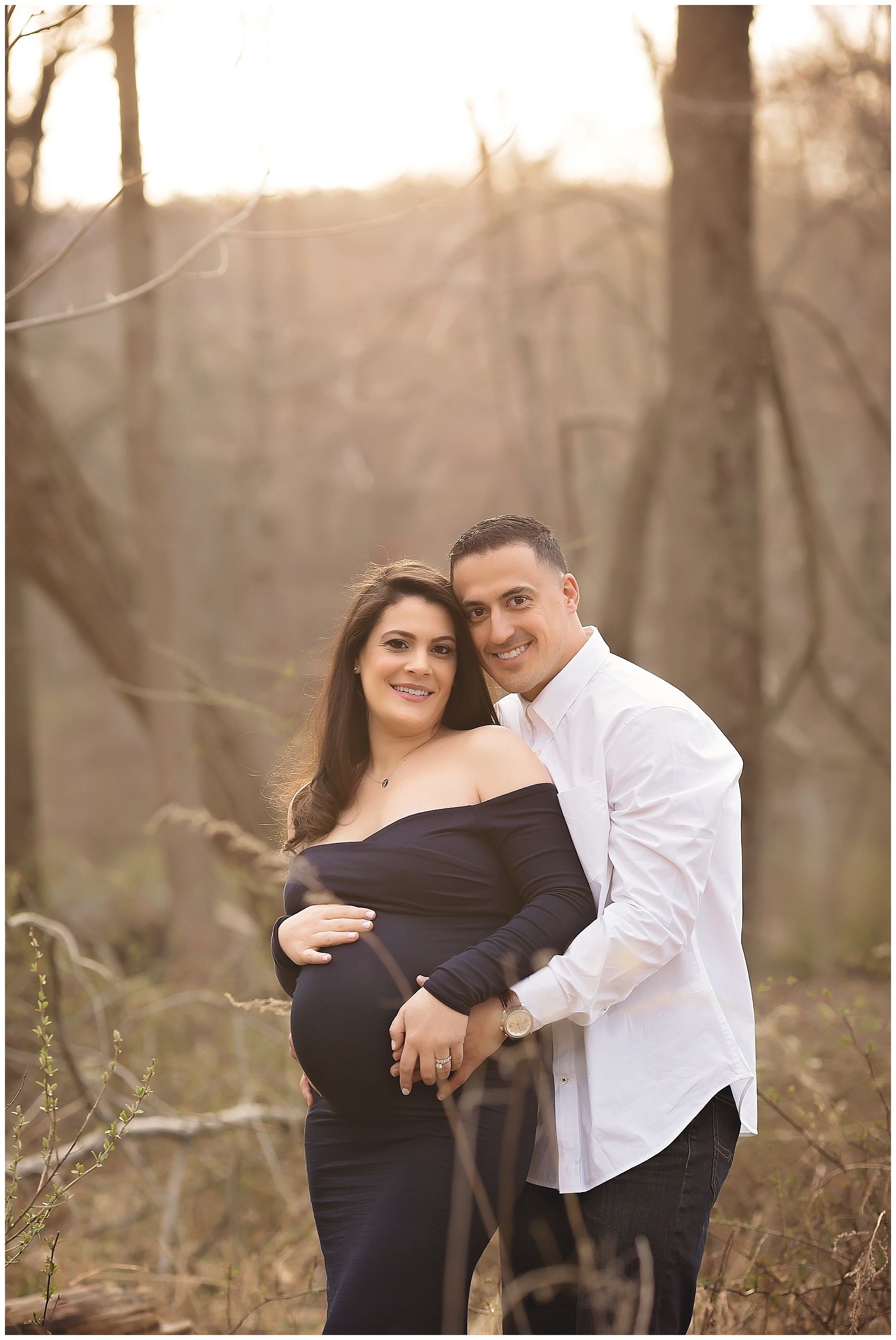 A man and a pregnant woman are posing for a picture in the woods.