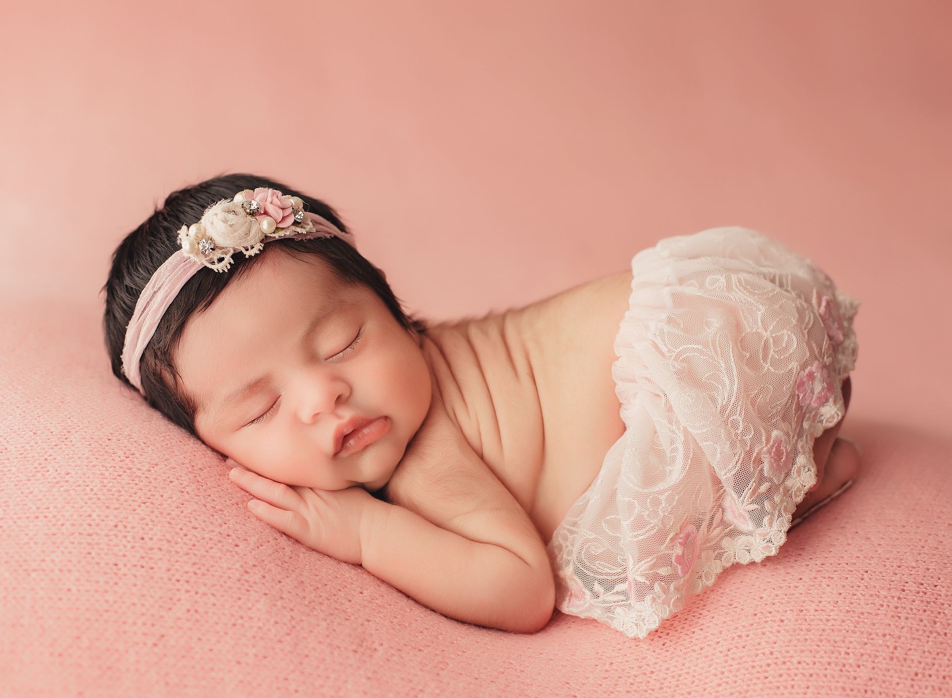 A newborn baby girl is sleeping on a pink blanket.