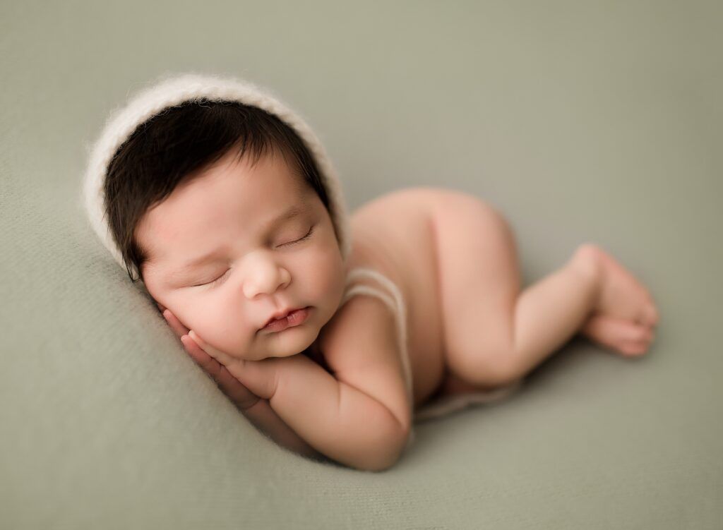 A newborn baby wearing a white hat is sleeping on a green blanket.