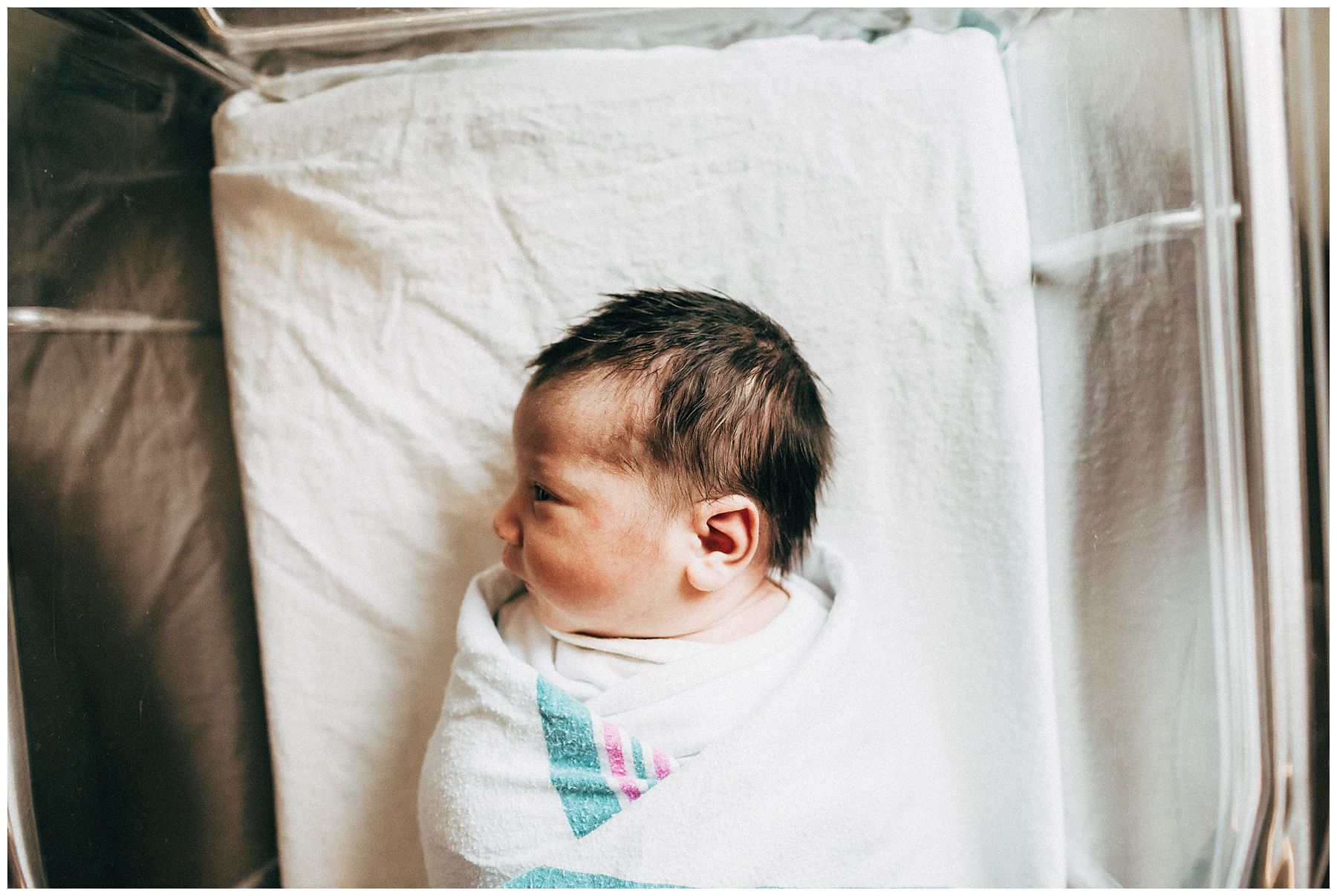 A newborn baby wrapped in a blanket is laying in a hospital bed.