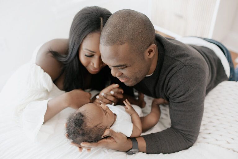 A man and woman are laying on a bed holding a baby.