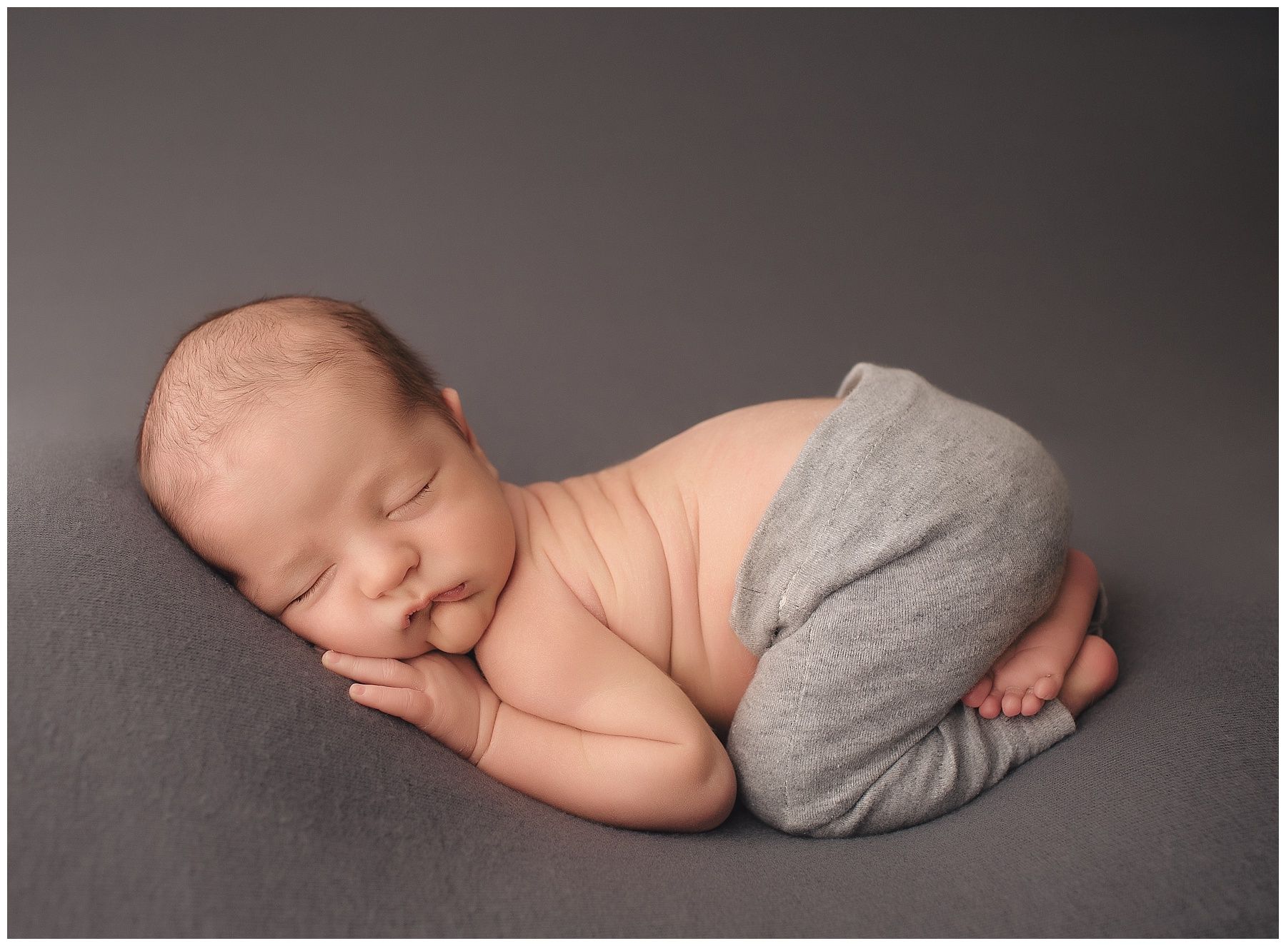 A newborn baby is sleeping on a gray blanket.