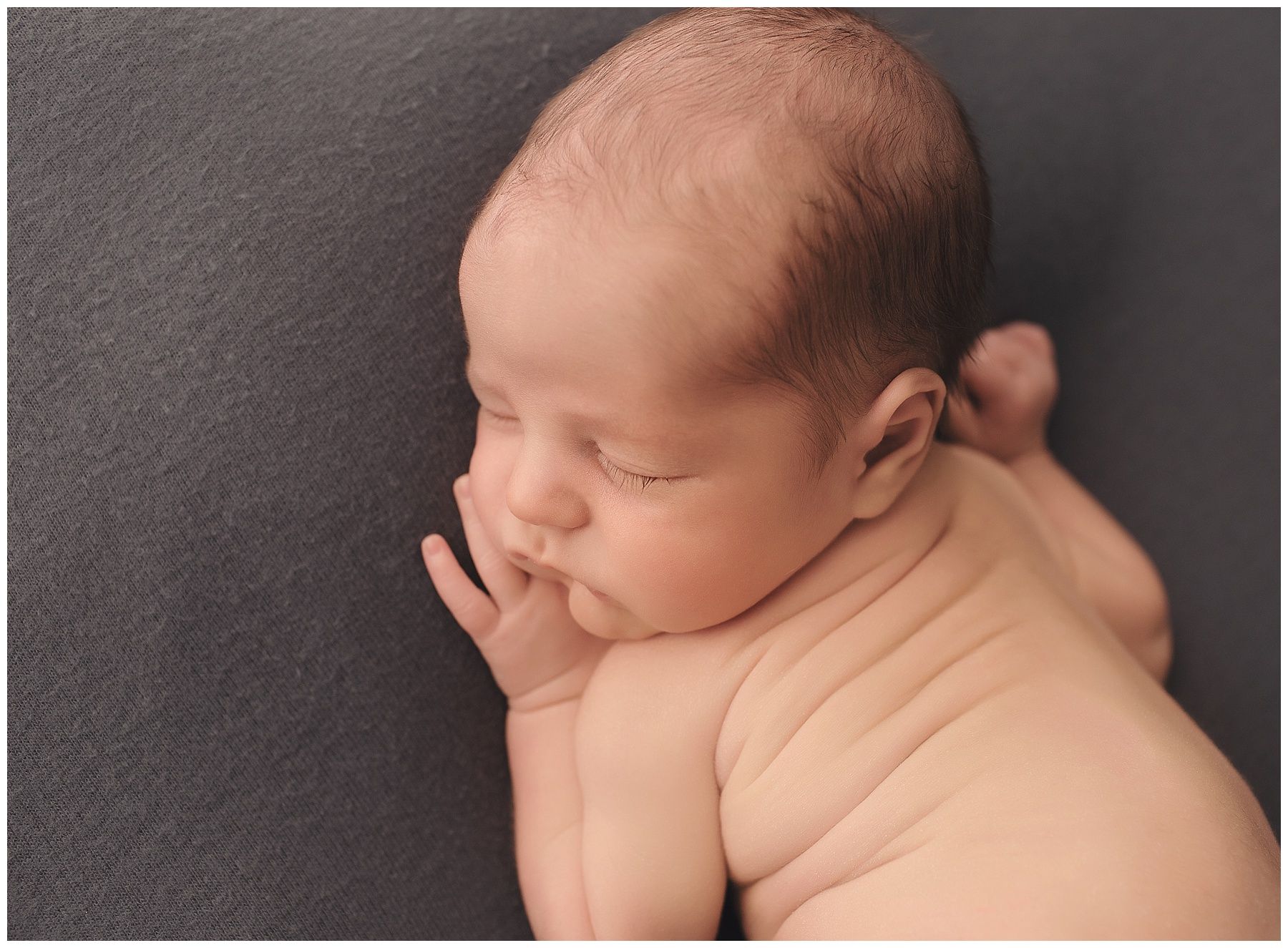 A newborn baby is sleeping on a gray blanket.