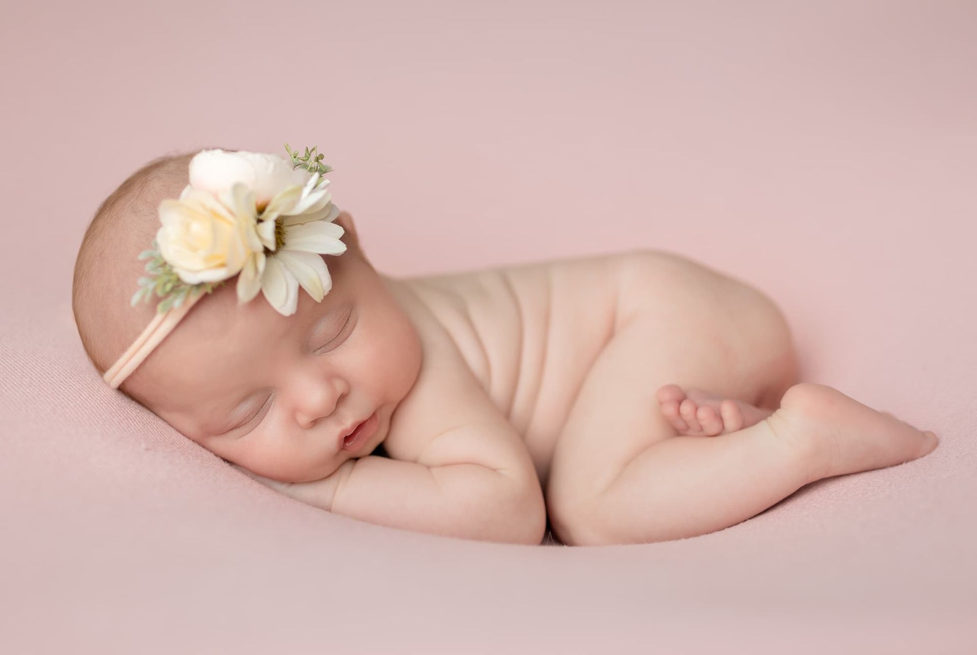 Newborn baby sleeping on pink blanket, wearing floral headband.