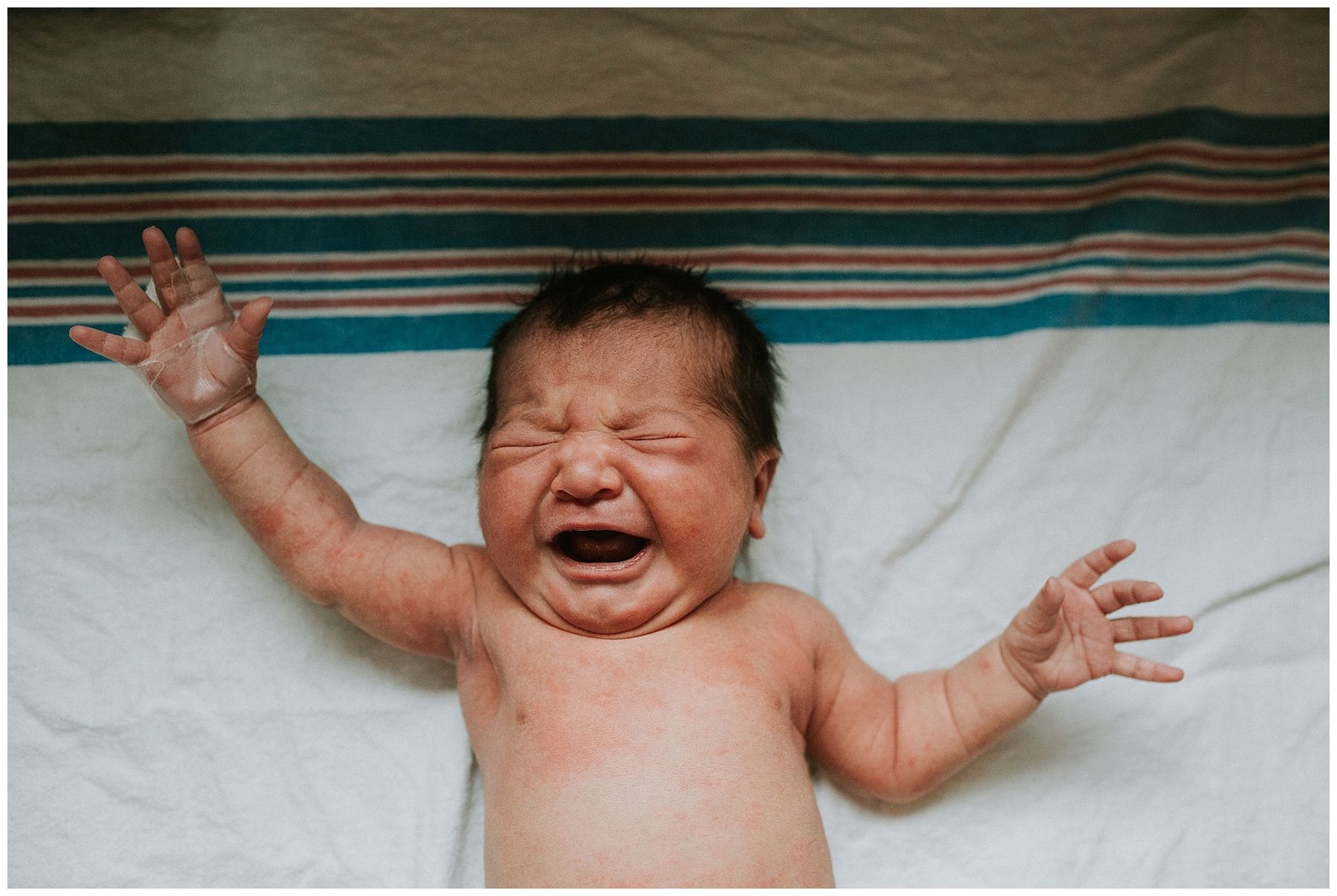 A newborn baby is crying while laying on a bed.