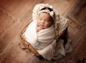 A newborn baby wrapped in a white blanket is sleeping in a wicker basket.