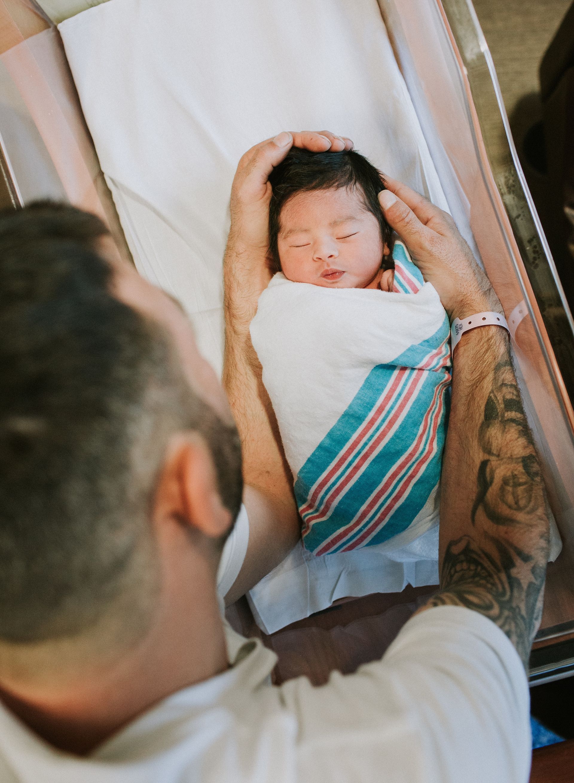 A man is holding a newborn baby wrapped in a striped blanket.