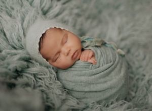 A newborn baby is wrapped in a blanket and wearing a hat.