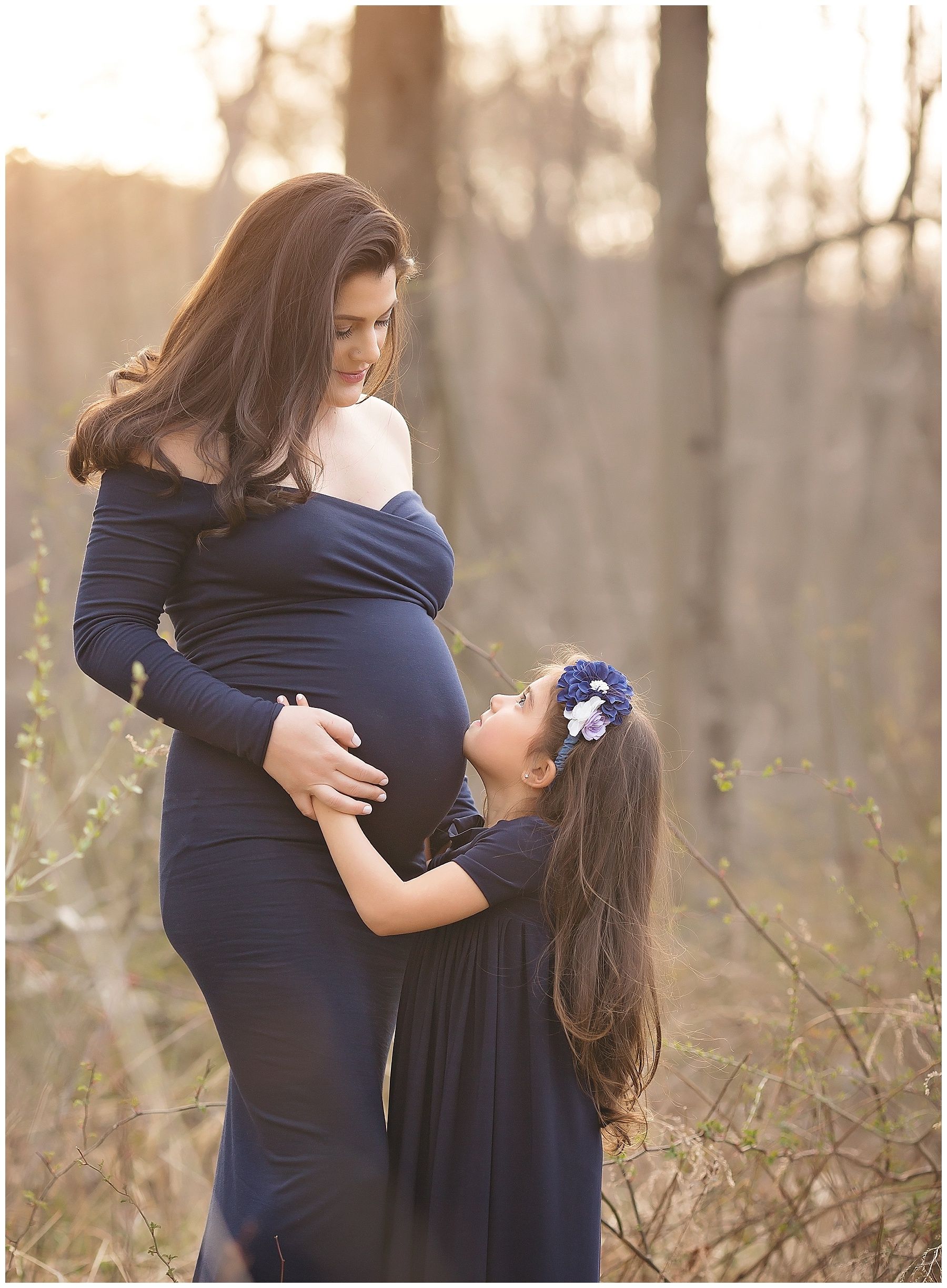 A pregnant woman in a blue dress is standing next to a little girl in a blue dress.