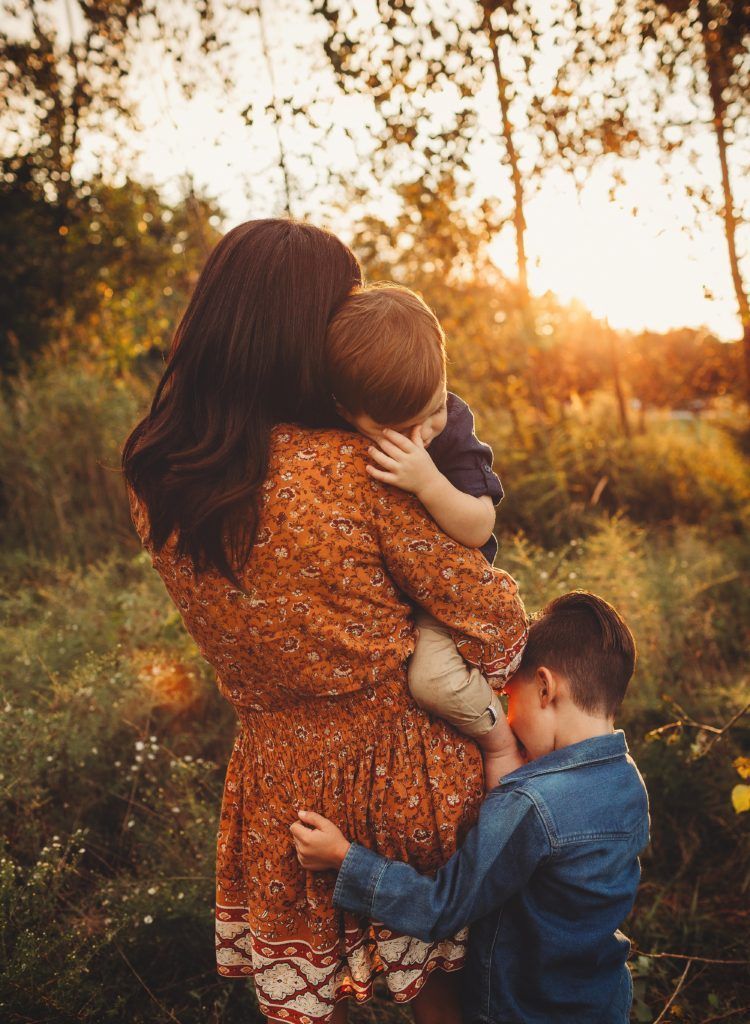 A woman is holding two children in her arms in a field.