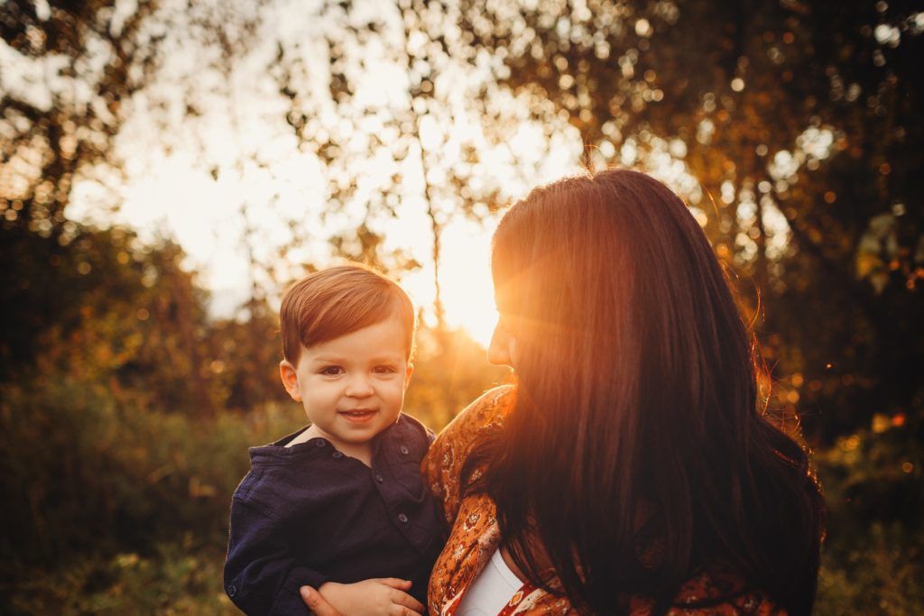 A woman is holding a little boy in her arms in a field at sunset.