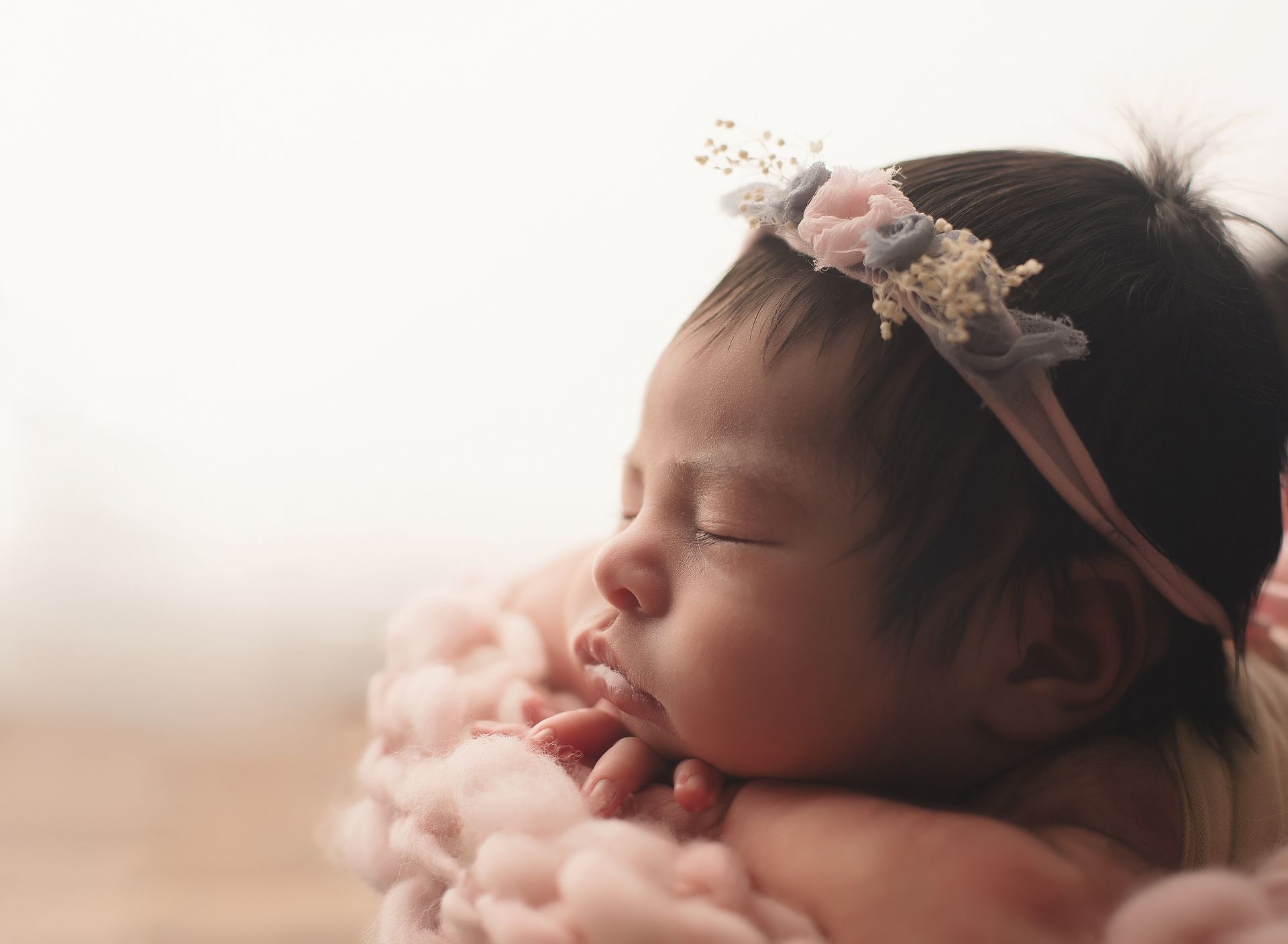 A newborn baby girl wearing a headband is sleeping on a pink blanket.